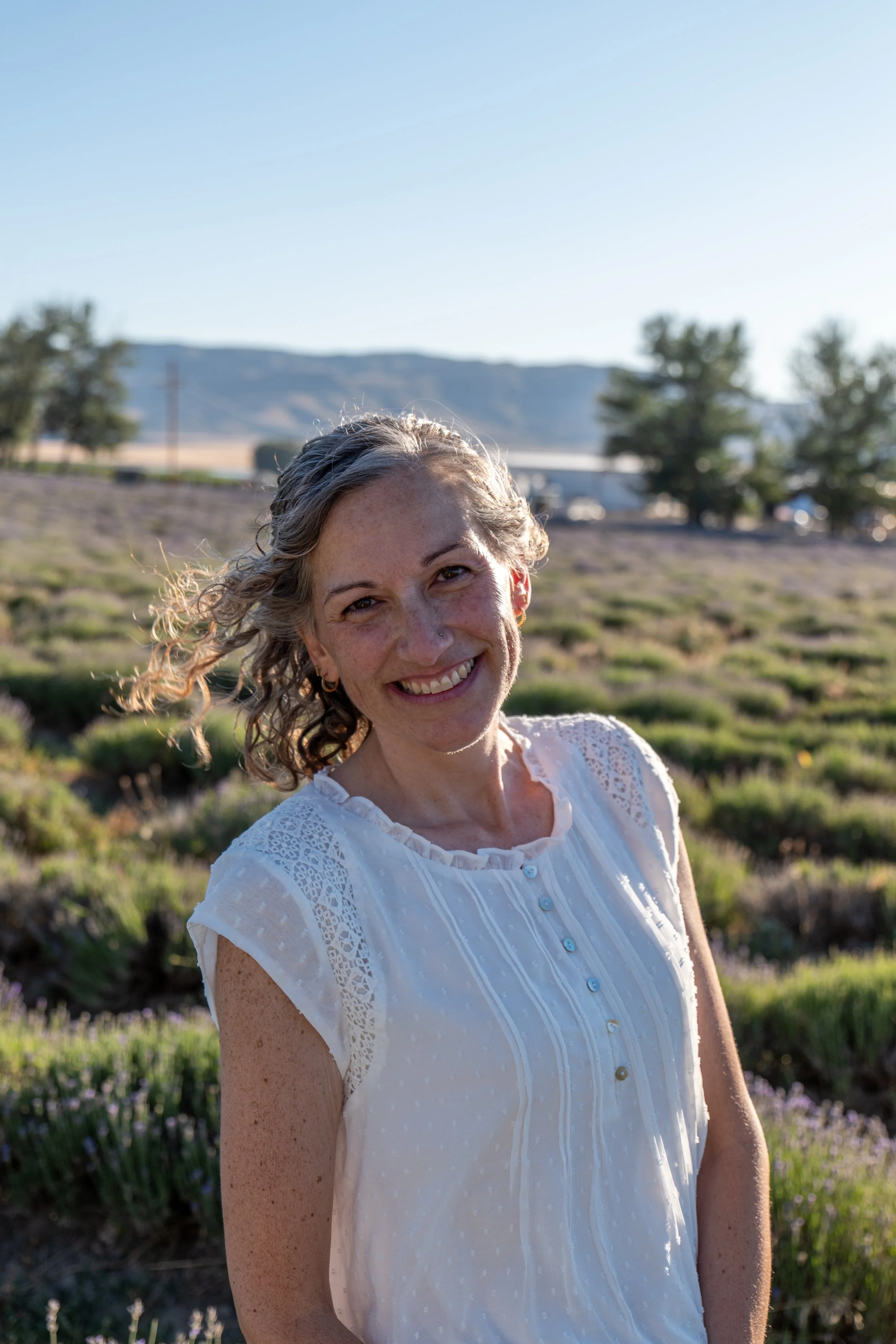 Smiling person with curly hair wearing a black top in front of a textured wall.
