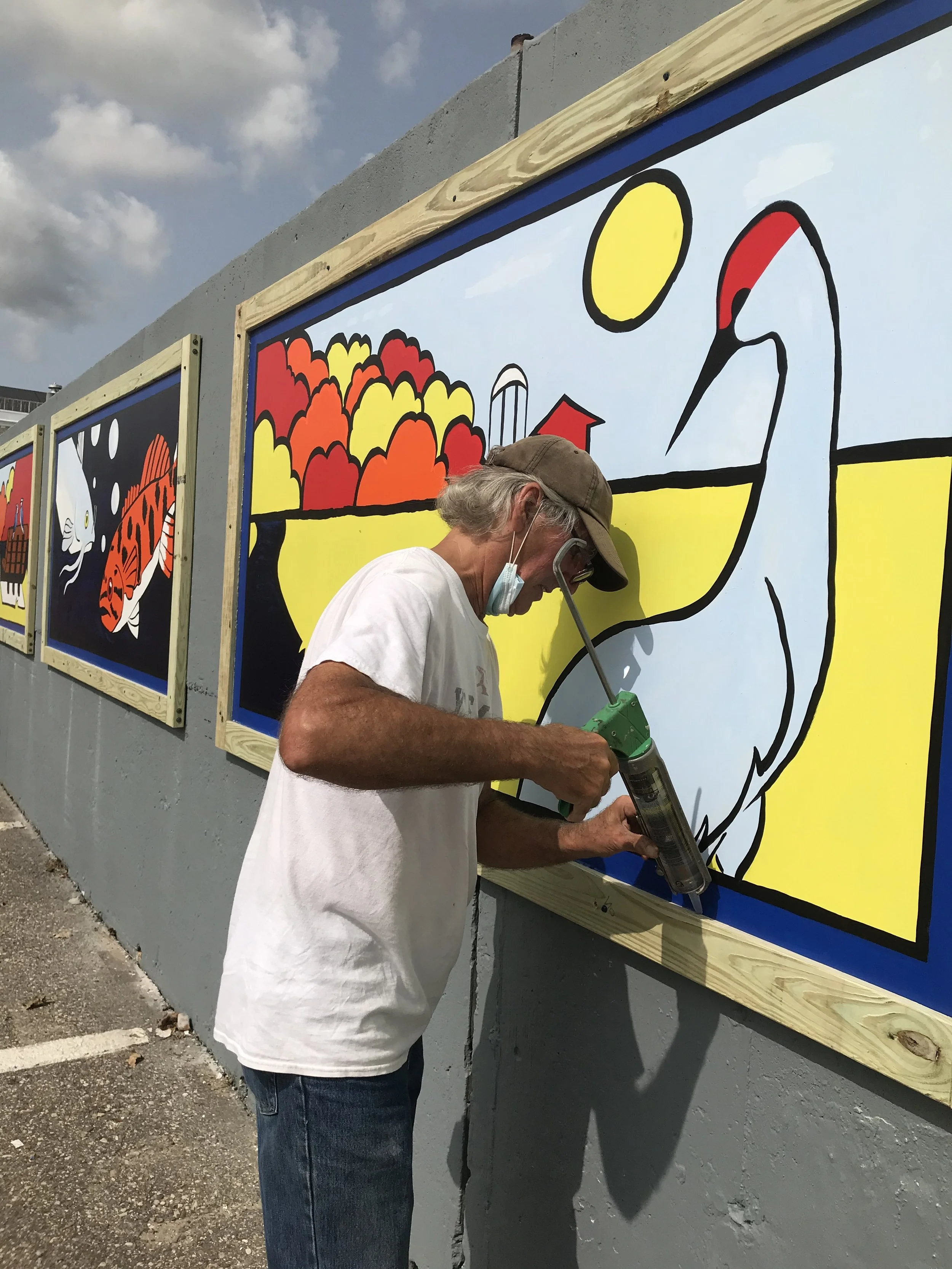 Man working on completing colorful outdoor mural painting of a swan on a wall