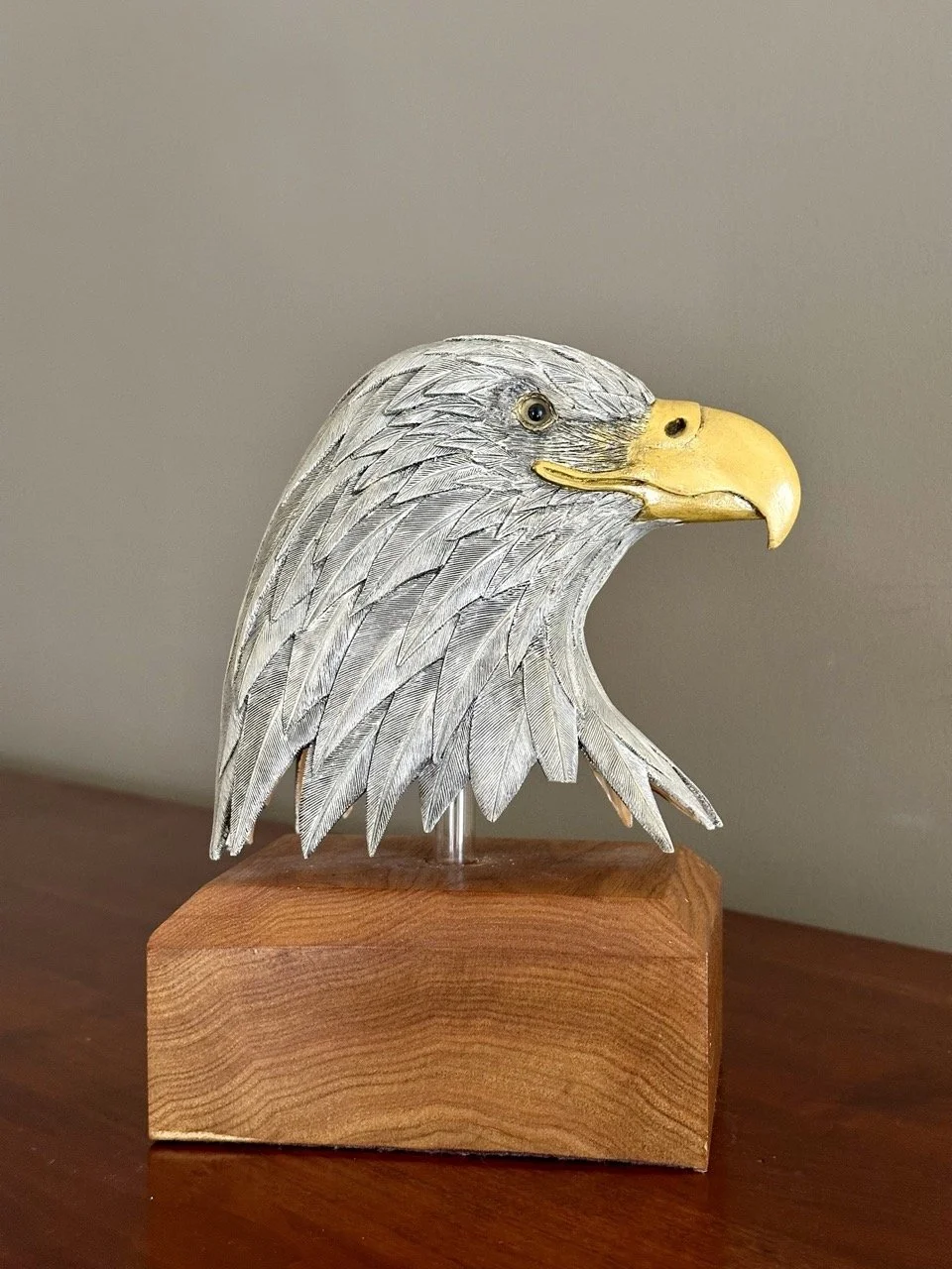 $35 • Hand-Carved Wooden Eagle Head Sculpture on Base • Detailed carved eagle head with painted beak and textured feather work mounted on wood base, rustic Americana décor piece with visible craftsmanship • Dimensions: 9” H x 7” W x 4.5” D (minor fea