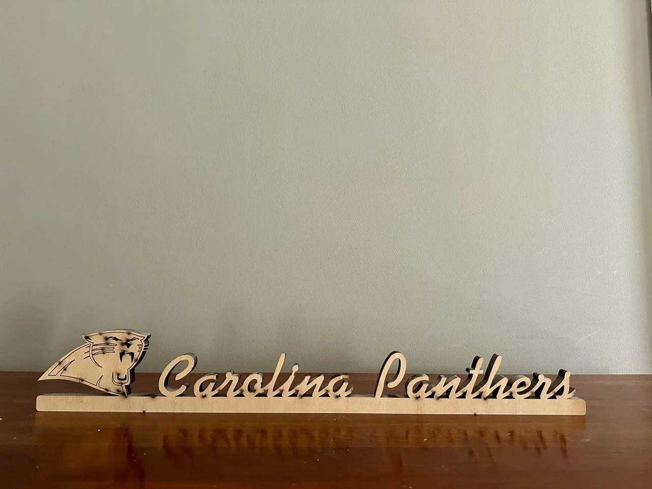 $25 • Carolina Panthers Wooden Script Sign with Logo • Lightweight wood display sign featuring Panthers logo and script lettering, great for shelf, wall, or fan space décor • Dimensions: 25.5” L x 4” H x 0.75” D (small chip on letter “A” noted)