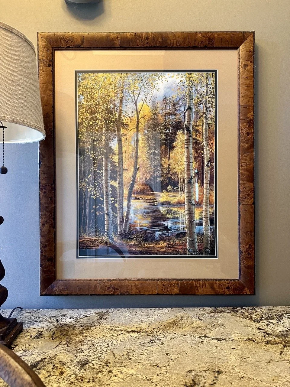 $120 - Framed Autumn Landscape Print (27.5” x 33.5”) | Large custom-framed autumn landscape print featuring a river scene with golden foliage. Real wood frame with burl-style finish and double matting. Excellent condition.