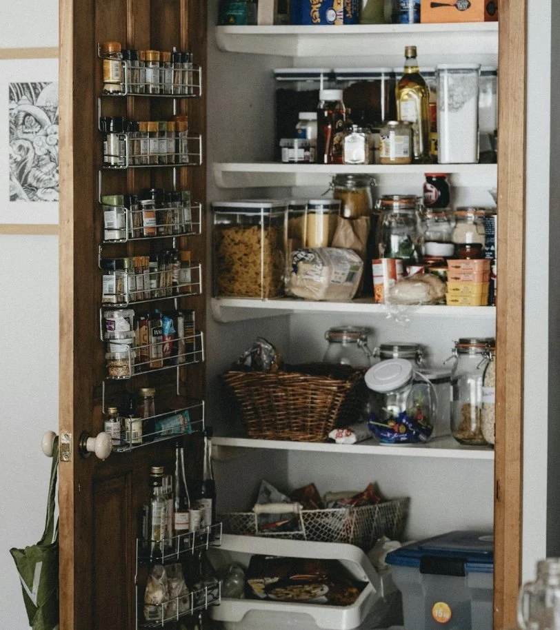 Inside a pantry closet with spices, jars, canned goods, and food containers on shelves and door racks.