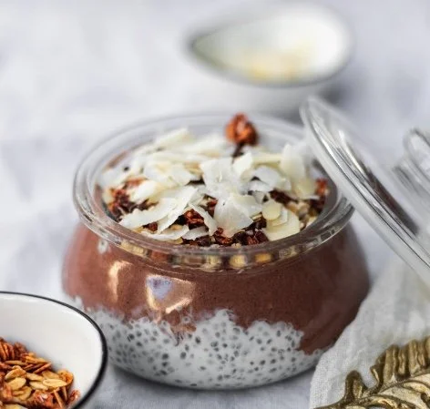 Layered chia seed pudding with chocolate and coconut flakes topped with white chocolate shavings in a glass jar.