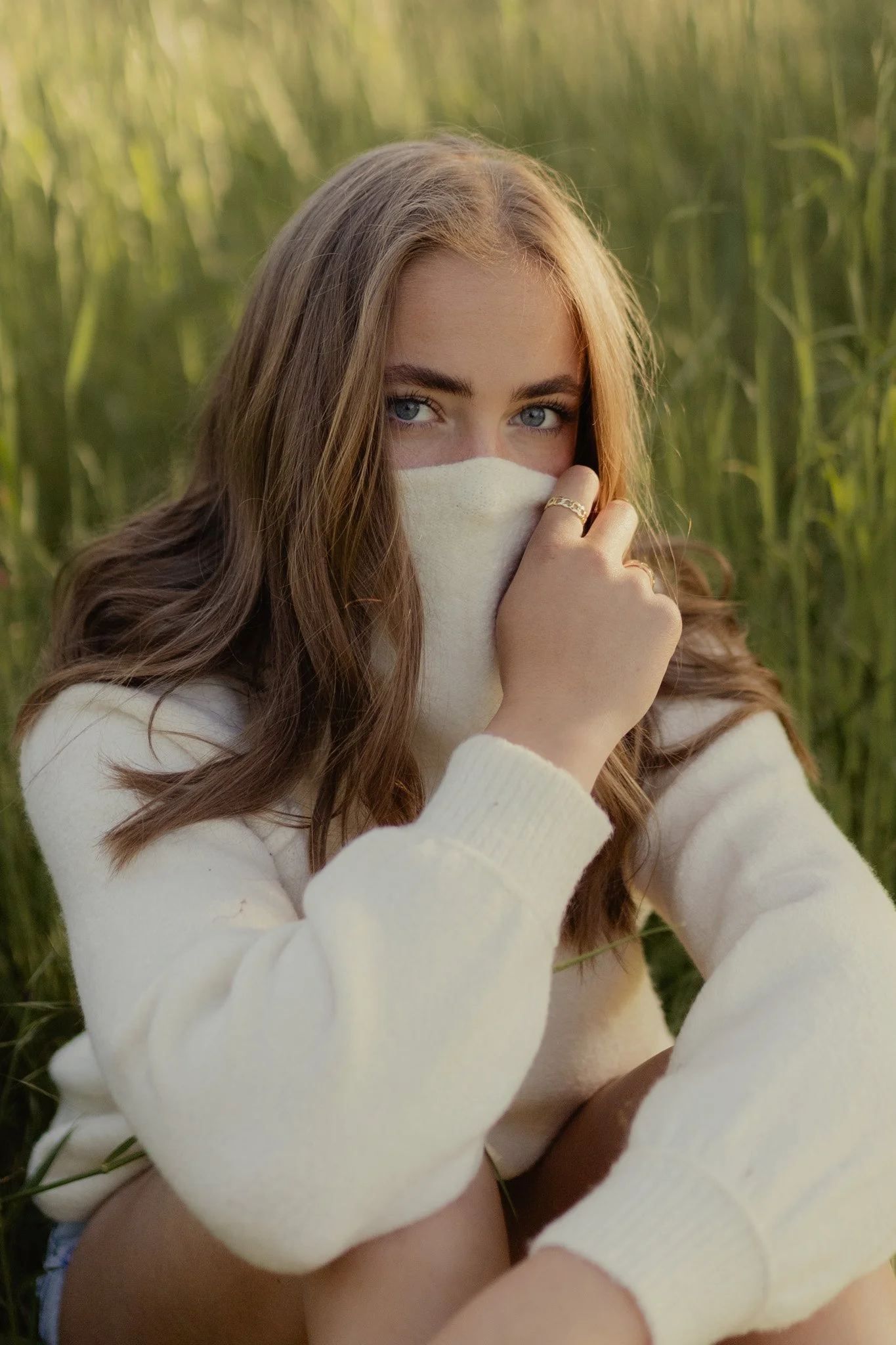 Senior covering her face with sweatshirt in tall grass at fort steilacoom park in steilacoom, Washington.