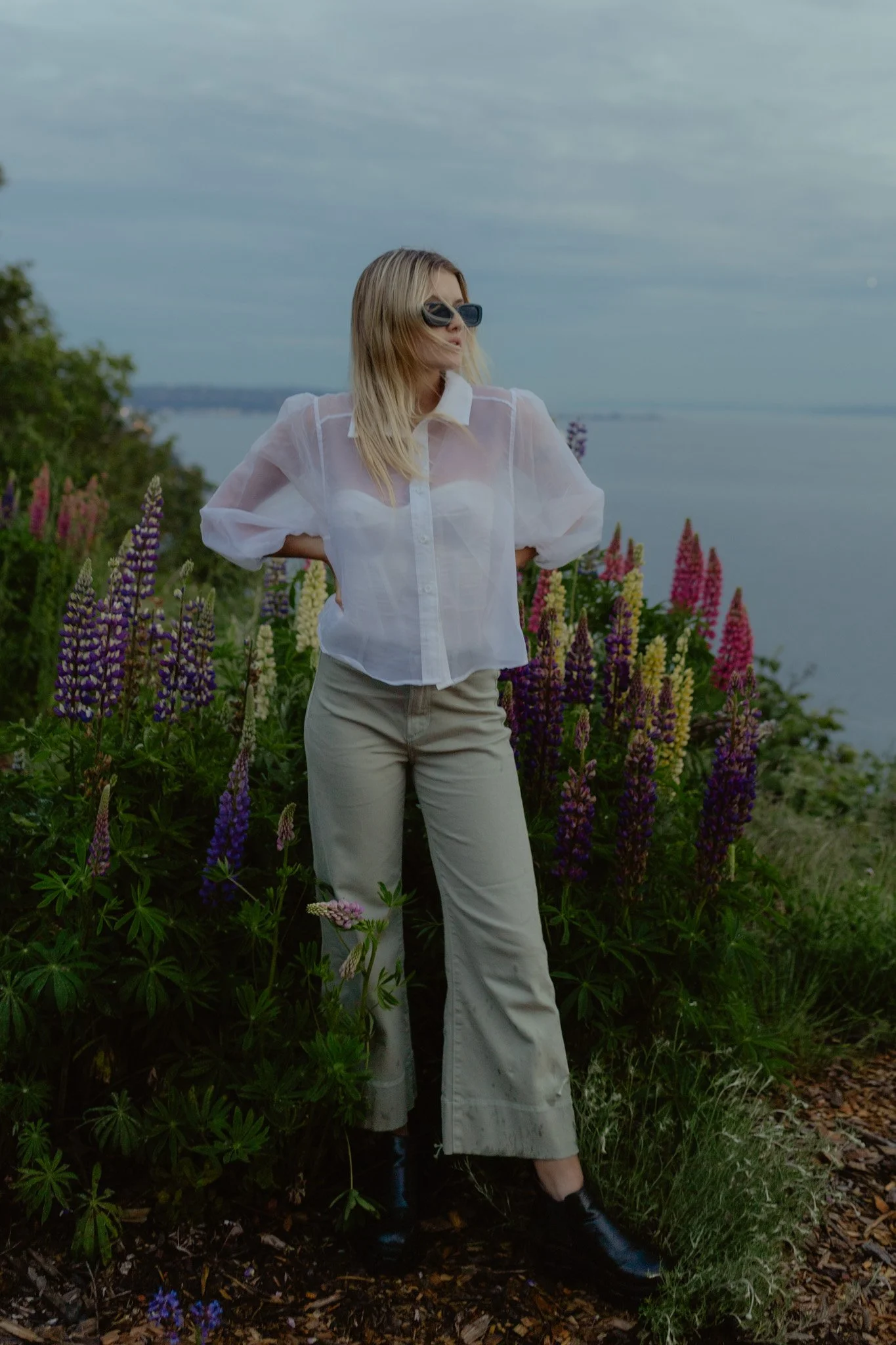 graduate standing in flowers in front of the ocean at discovery park in Seattle, Washington