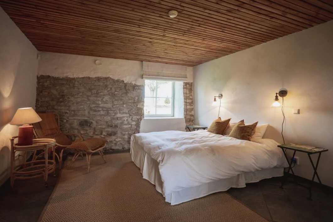 A cozy bedroom with a bed that has blue pillows and a striped bedspread. There are nightstands with lamps and a window with curtains in a wooden-paneled, A-frame style room.