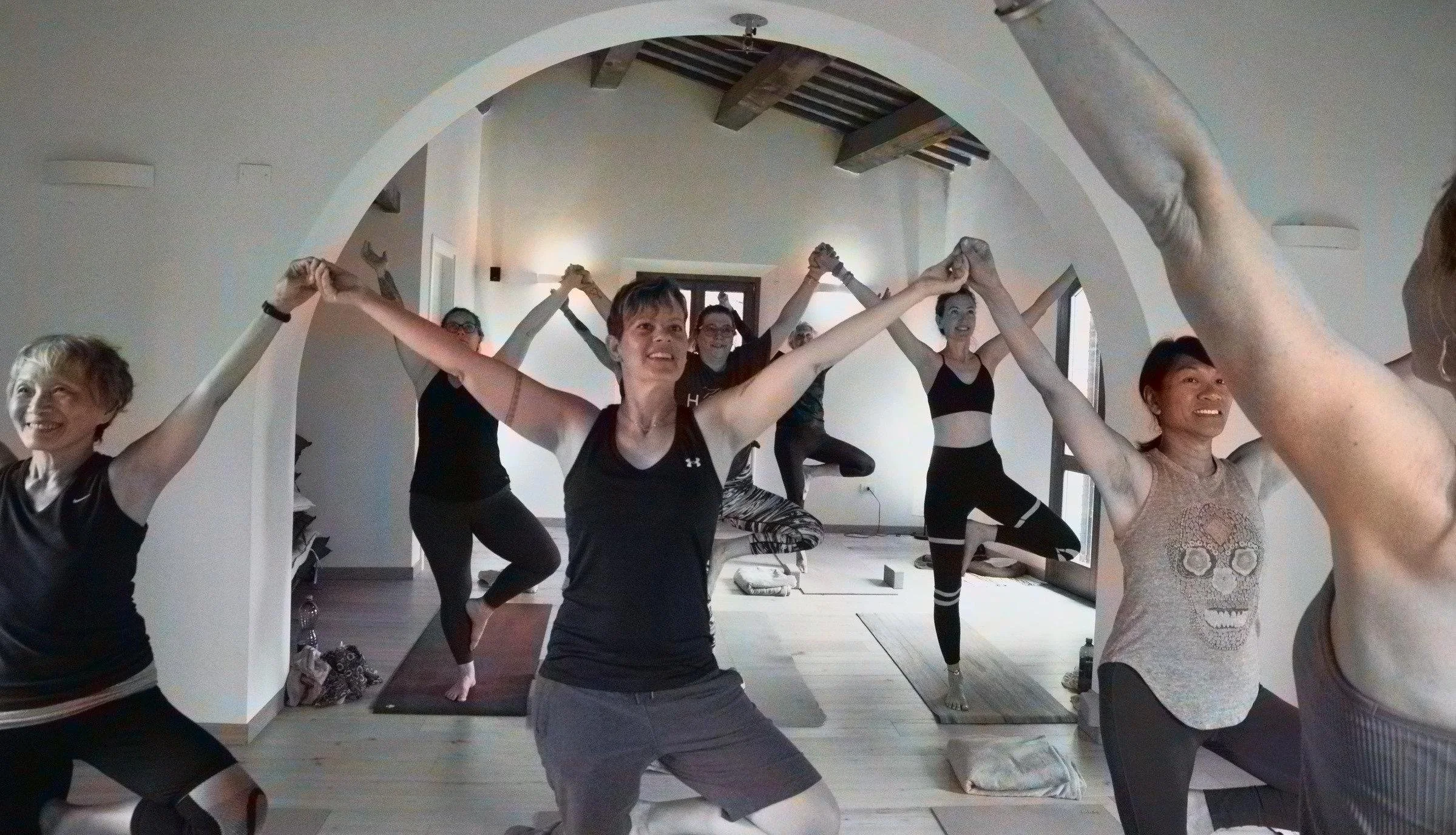 A group of people participating in a yoga or meditation class in a cozy, sunlit room with wooden floors and large windows.