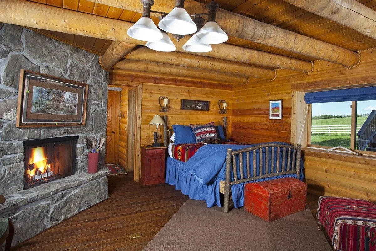 A cozy bedroom with a bed that has blue pillows and a striped bedspread. There are nightstands with lamps and a window with curtains in a wooden-paneled, A-frame style room.