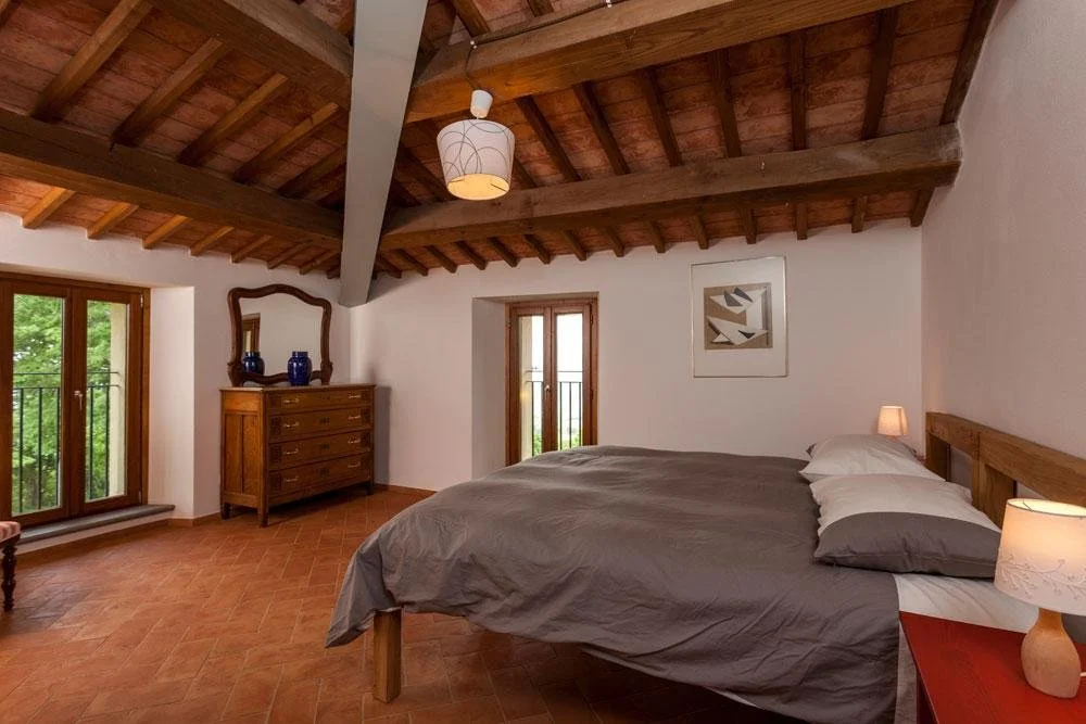 A cozy bedroom with a bed that has blue pillows and a striped bedspread. There are nightstands with lamps and a window with curtains in a wooden-paneled, A-frame style room.