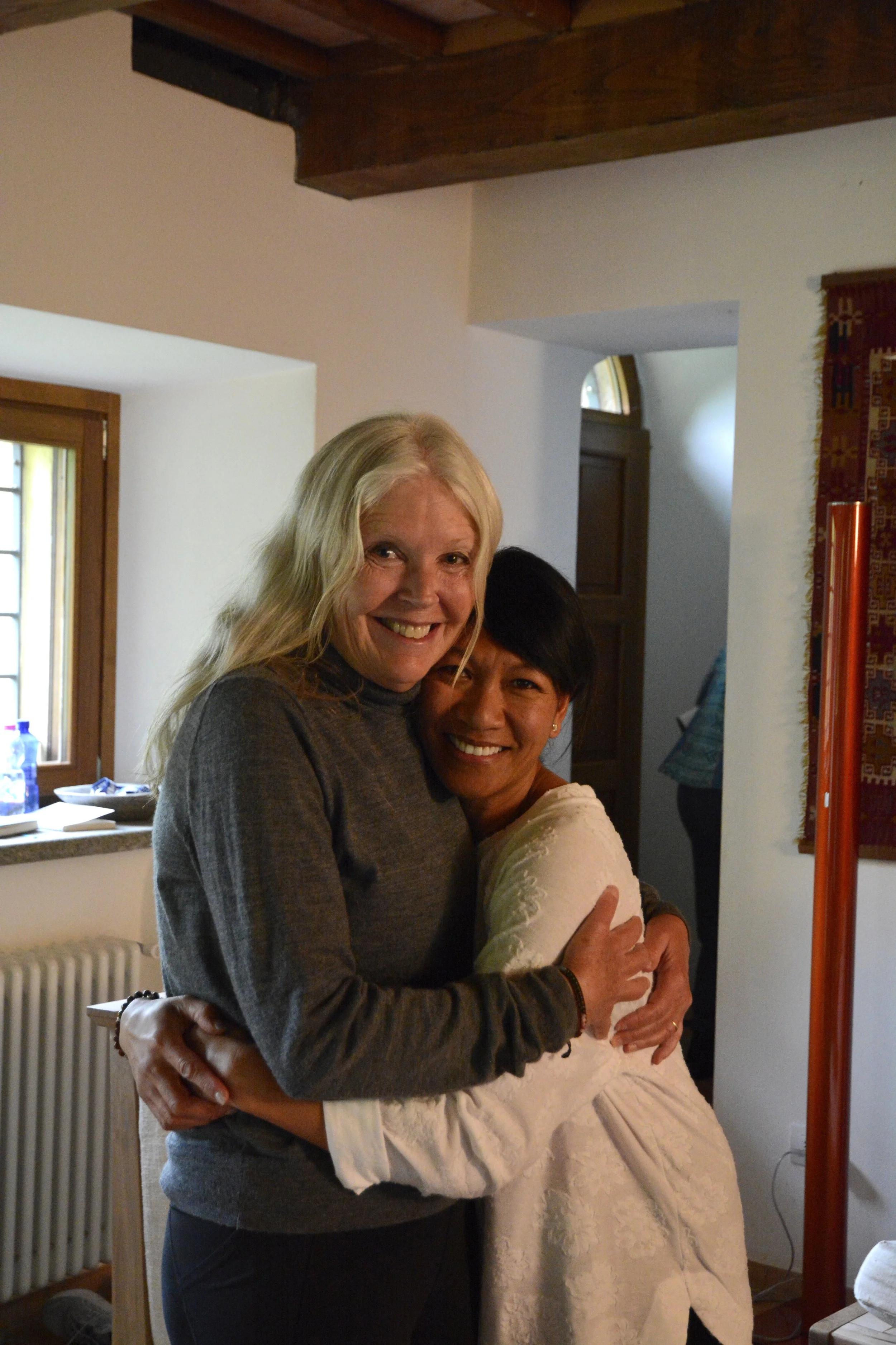 A group of people participating in a yoga or meditation class in a cozy, sunlit room with wooden floors and large windows.