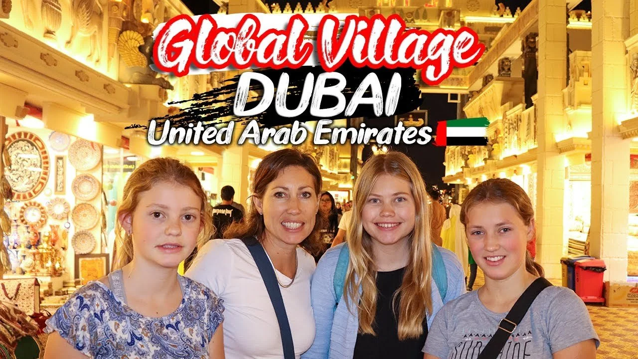 A group of four smiling girls and a woman standing together in a brightly lit marketplace in Dubai, United Arab Emirates, with decorative arches and goods in the background.