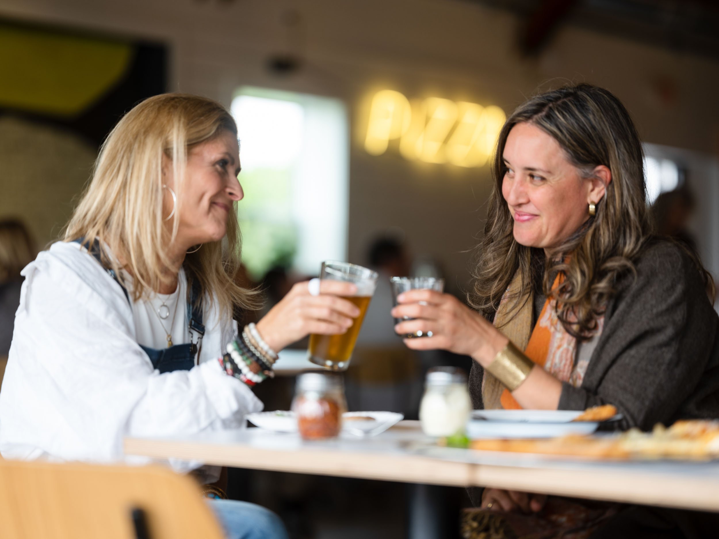 Two women smile while toasting glasses of beer