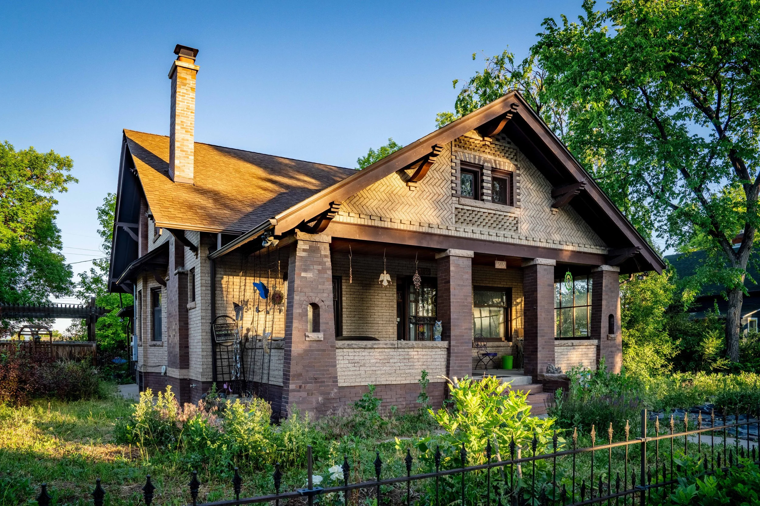 A charming two-story house with a brick exterior, gabled roof, and front porch, surrounded by green trees and a garden.