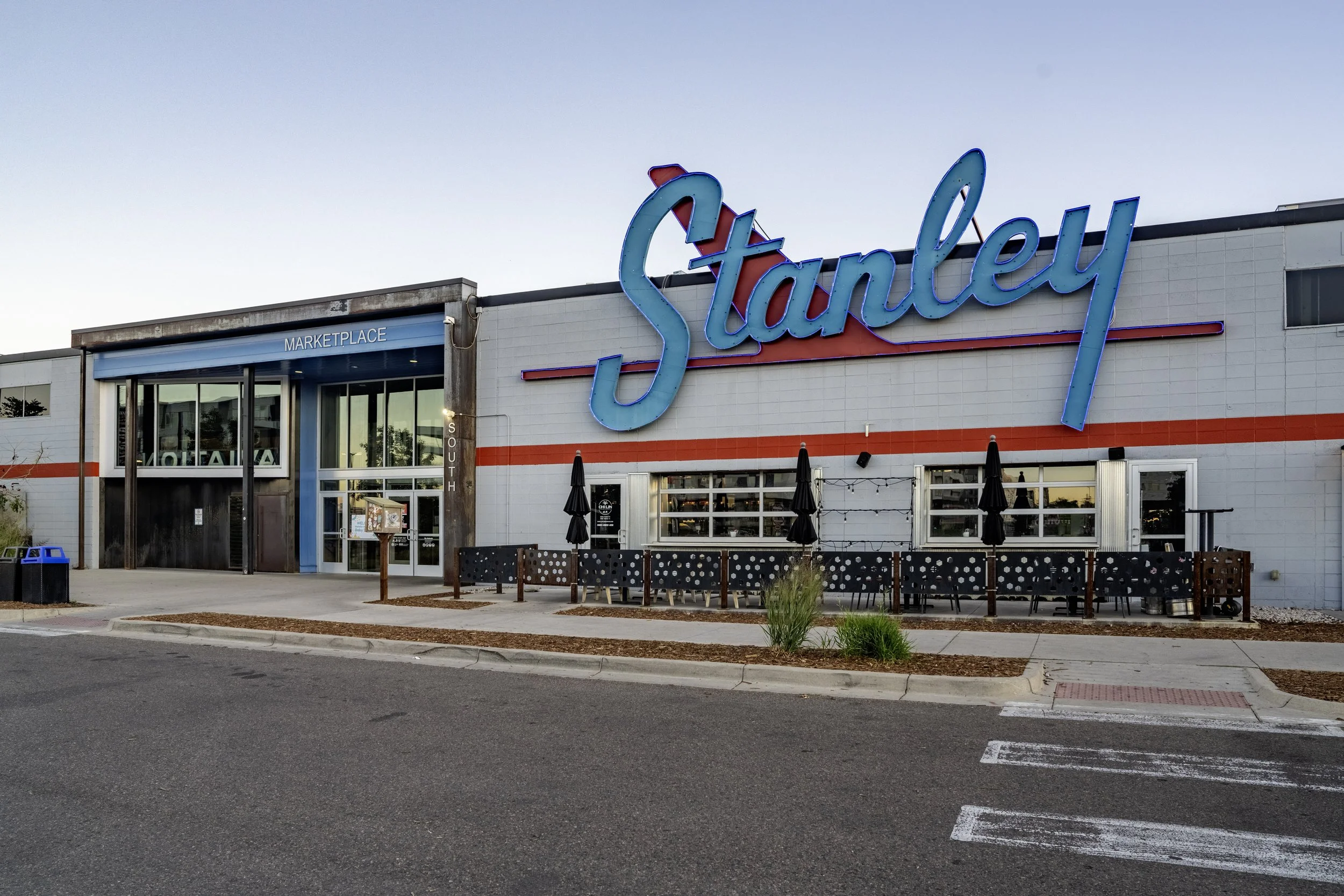 The exterior of Stanley, a retail store with a large neon sign of the store's name, with outdoor seating and umbrellas in front.