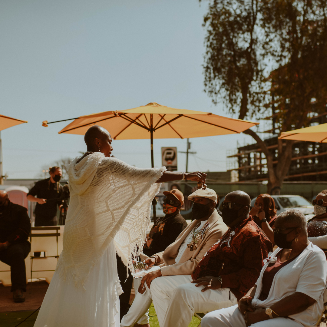 Onyi Love, priestess and facilitator, gives a blessing to a crowd under yellow umbrellas during a celebration of life ceremony