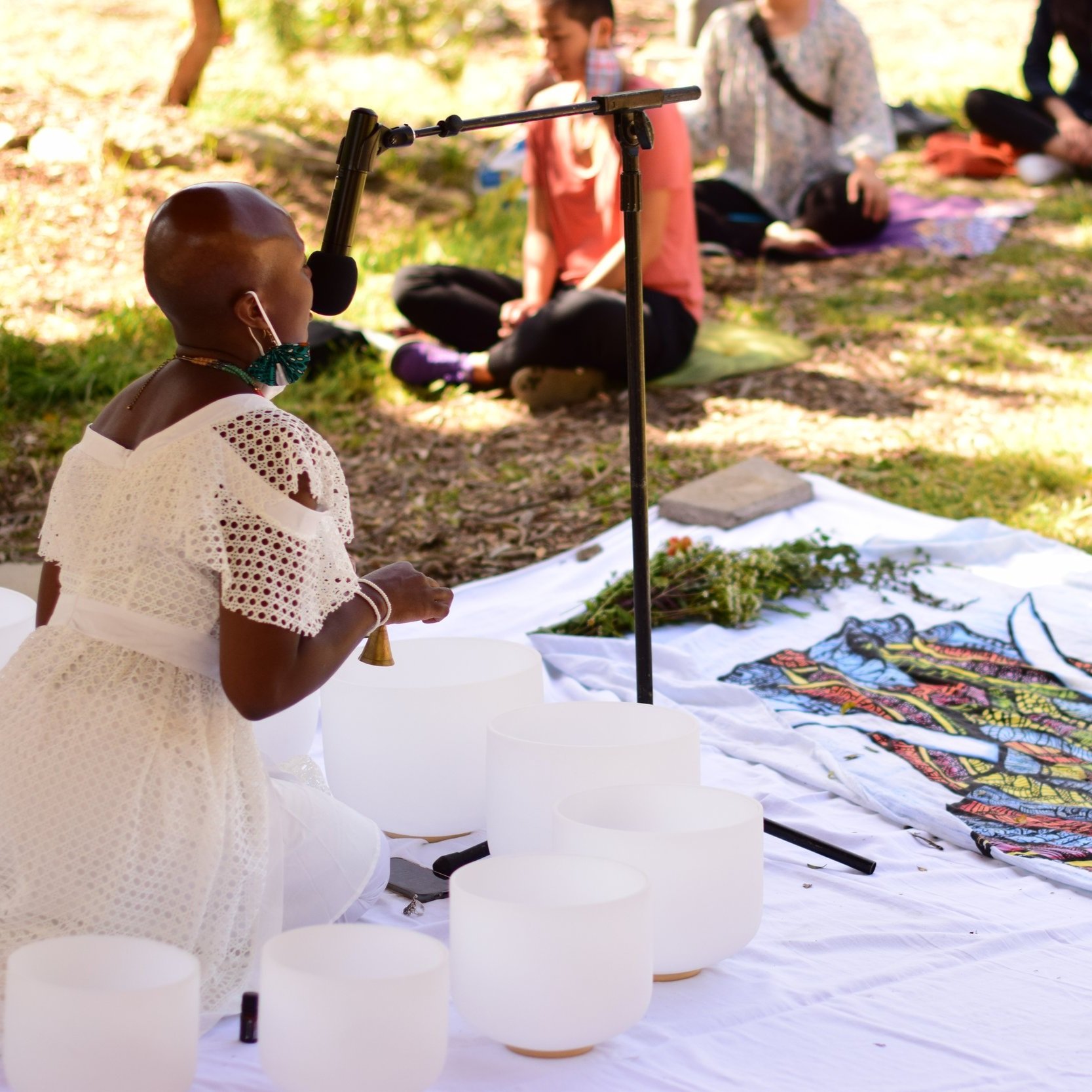 Onyi Love, sound healer and consultant, dressed in white conducting a sound immersion with crystal singing bowls at El Serreno Garden.
