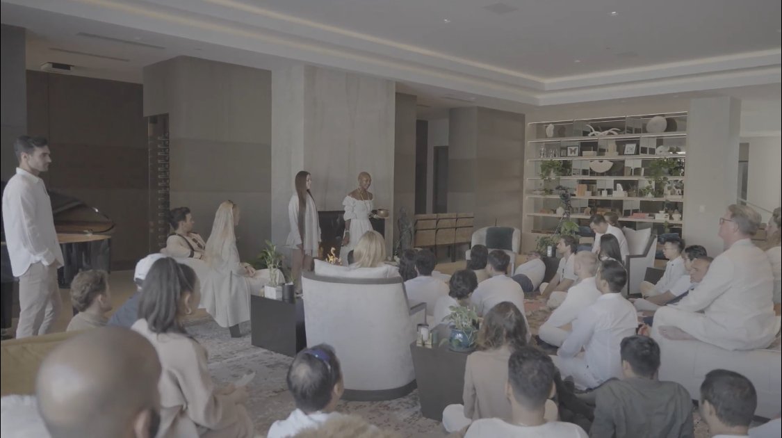 A group of people attending a spiritual gathering in a modern, well-lit lounge area, with Onyi Love and her colleague Christy leading meditation and talk.