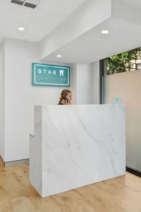 Reception area at a dental office with a white marble desk, a staff member on the phone, and a teal sign that says 'Star Dentistry' on the wall.