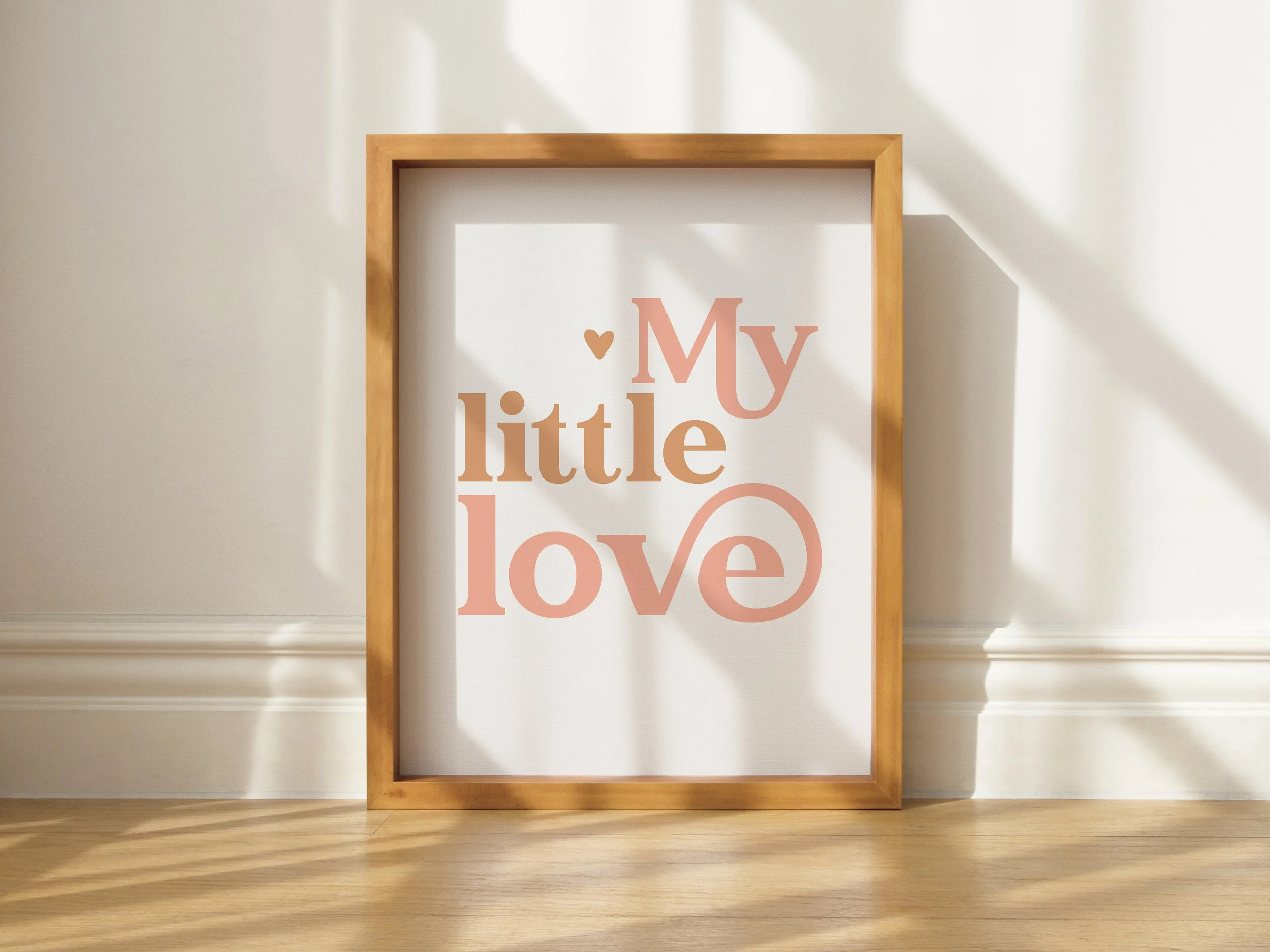Framed wall art with the words "My little love" in pink and brown letters, leaning against a white wall with sunlight and shadows.