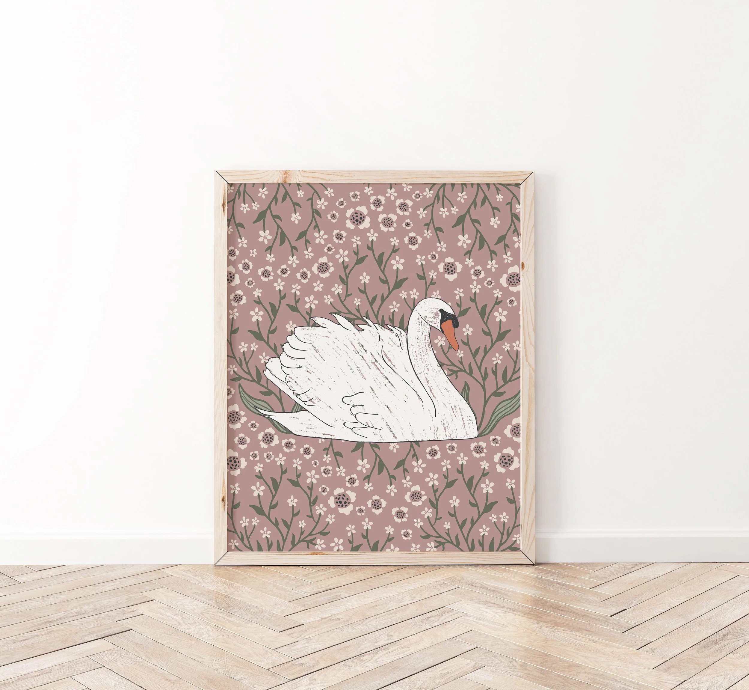 Framed artwork of a white swan with a pink background decorated with small white flowers and green leaves leans against a white wall on a wooden floor.