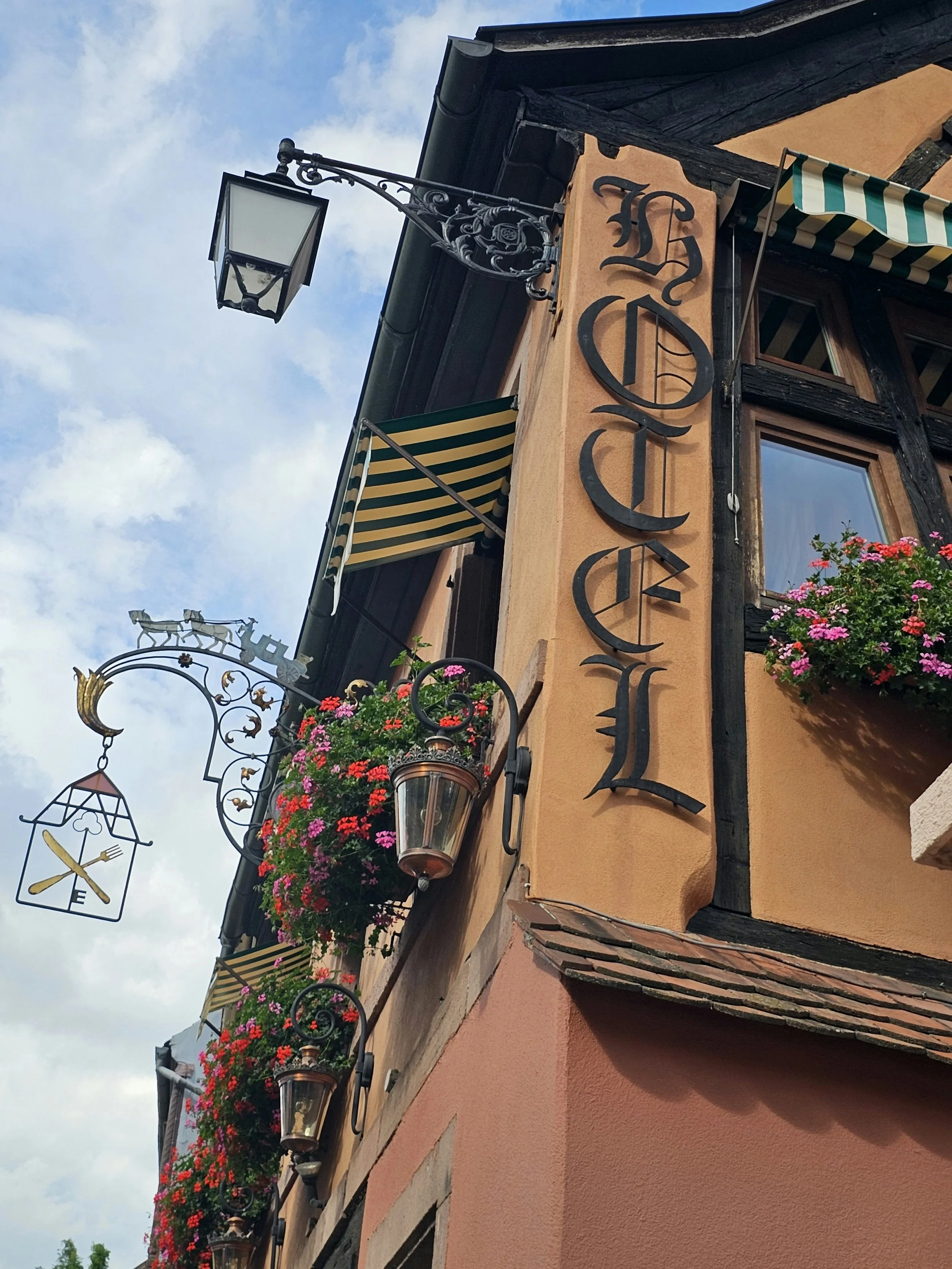 Hotel sign with hanging lanterns and flowers on a timber-framed building.