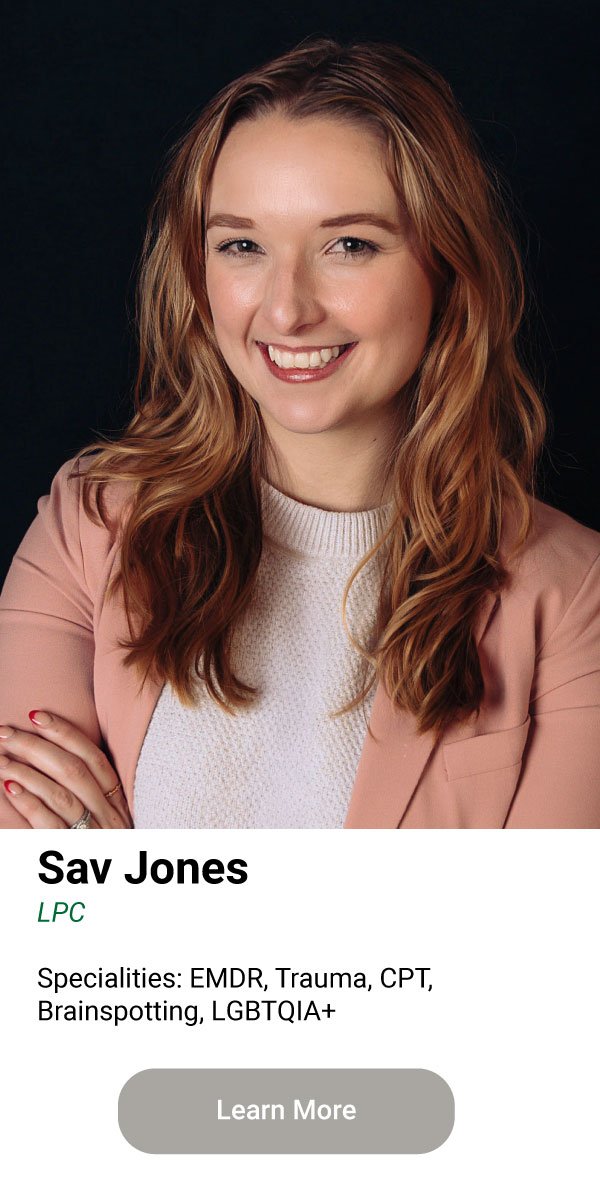 Headshot of a smiling woman with wavy, shoulder-length red hair, wearing a light pink blazer and a white top, against a dark background.