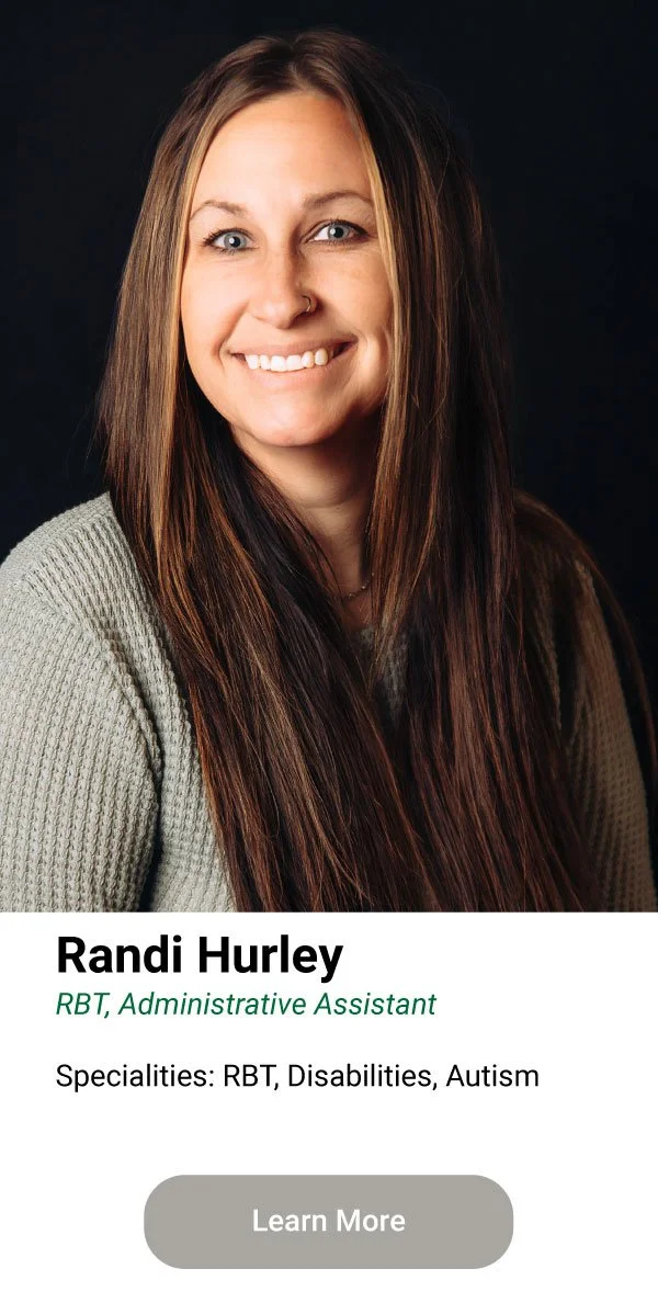 A woman with long brown hair, wearing a gray sweater, smiling against a dark background.