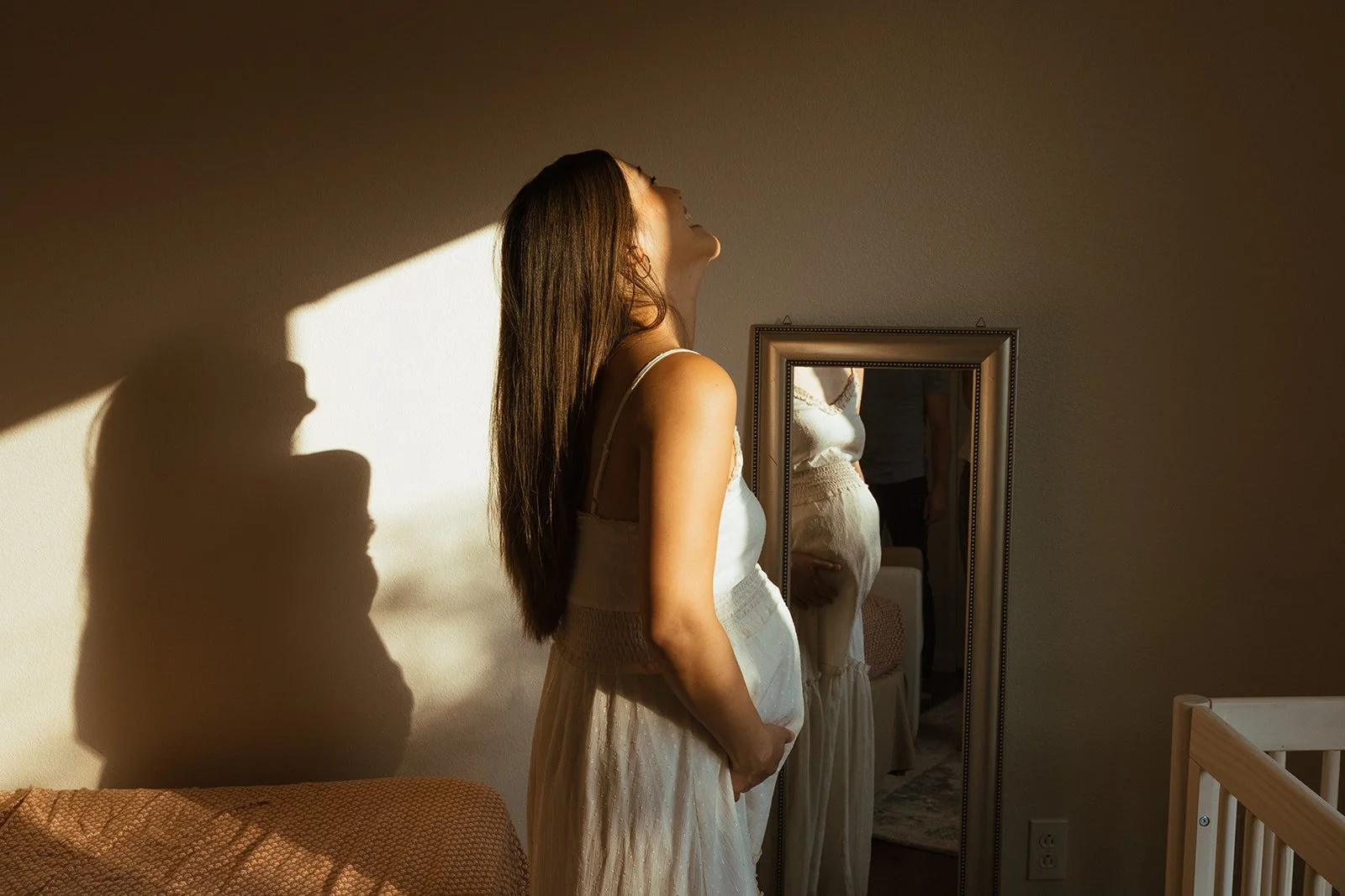 exuberant woman standing in front of mirror with sunlight casting shadow on wall.