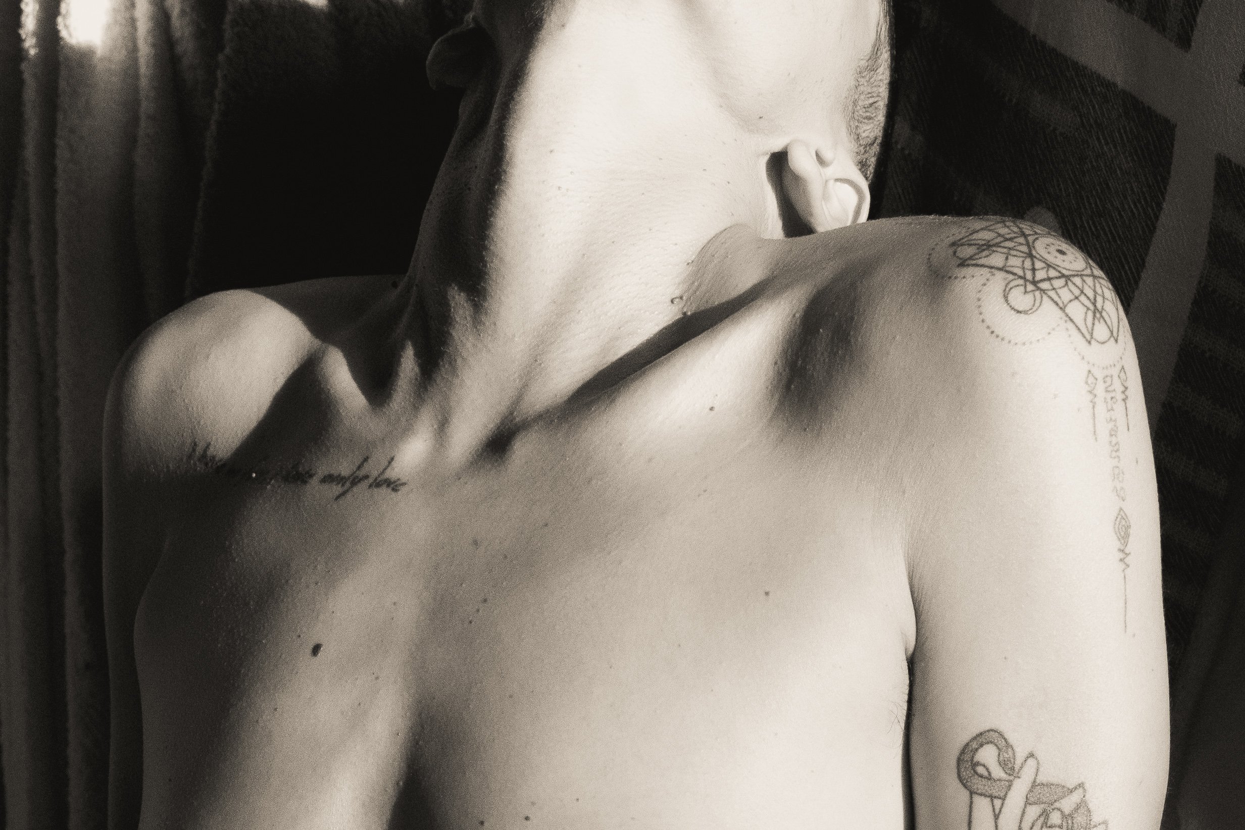 Close-up of an upper body with tattoos, showing the neck and shoulder area, photographed in black and white.