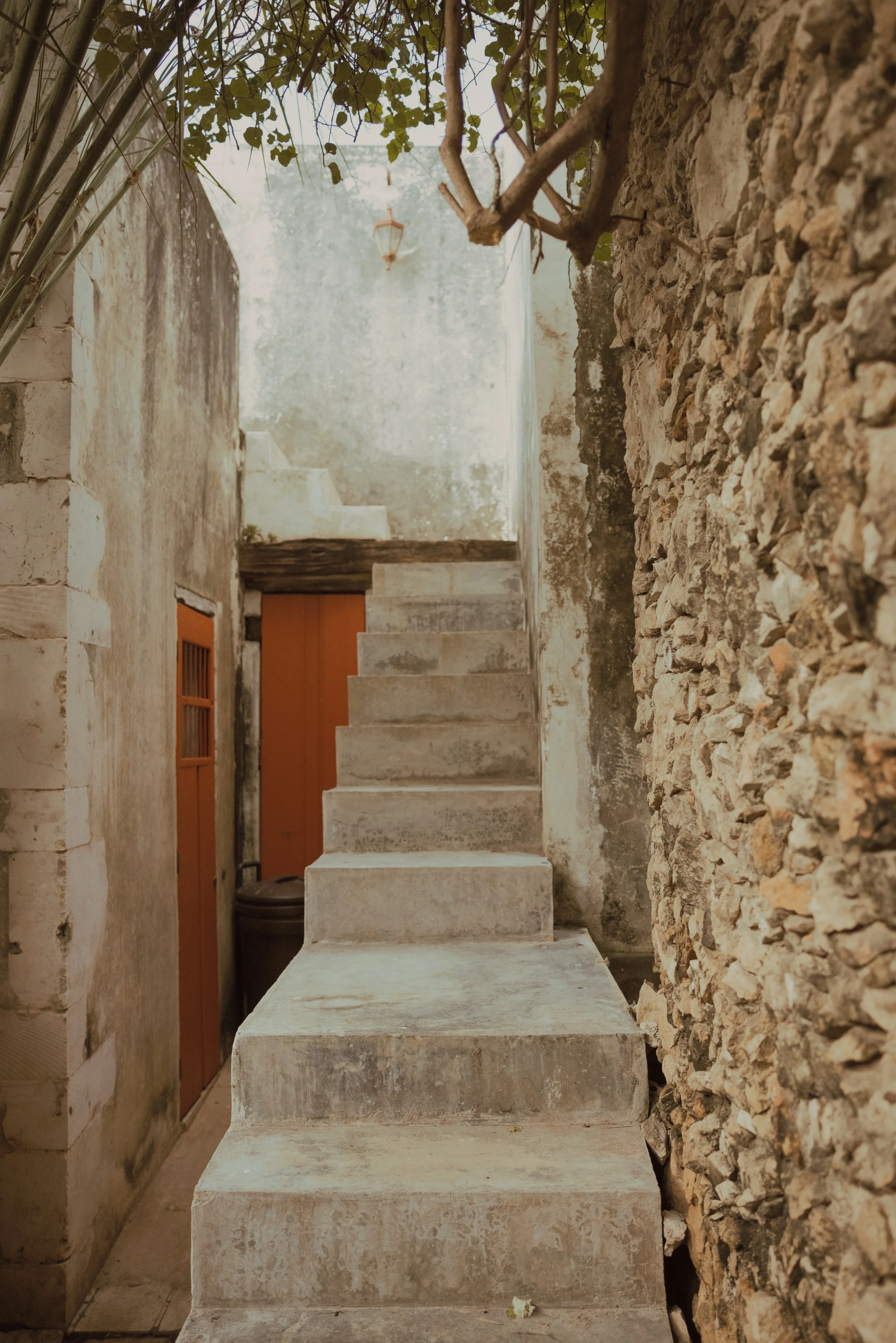 Stone staircase leading to an alluring upper level boutique hotel, surrounded by stone walls, and a bright orange door below.