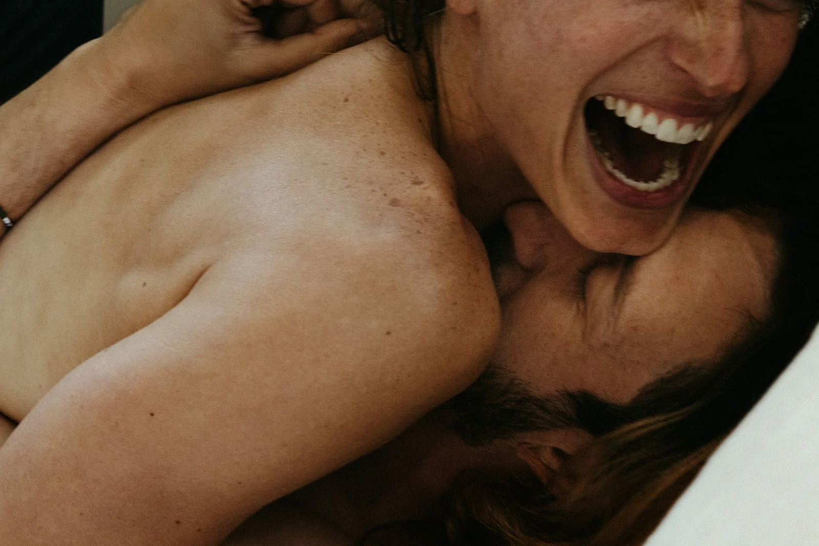 Close-up of a woman laughing with her mouth open, lying on top of a man.