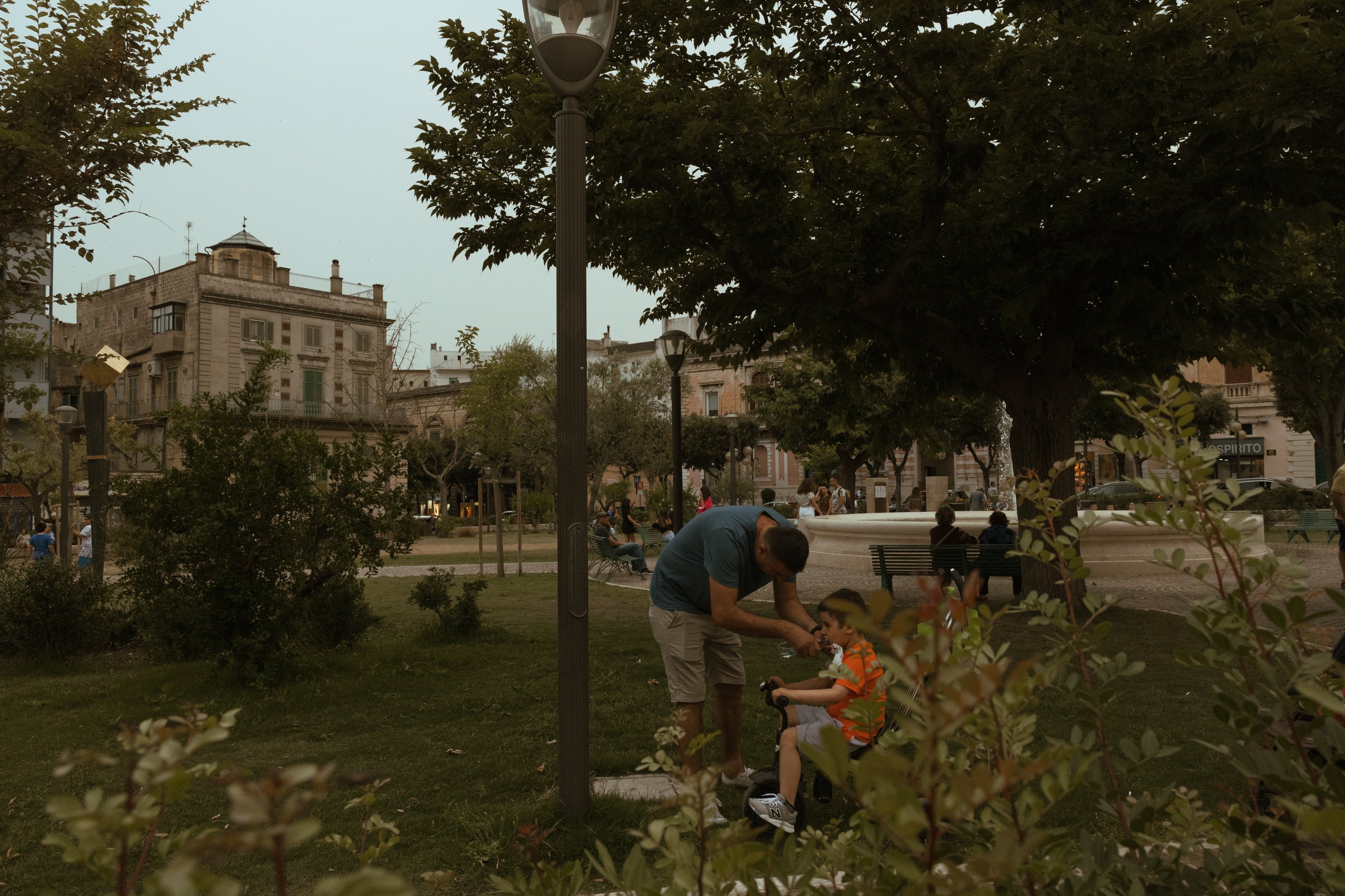 a parent feeding ice cream to a young child in a plaza with a vintage renaissance feeling 