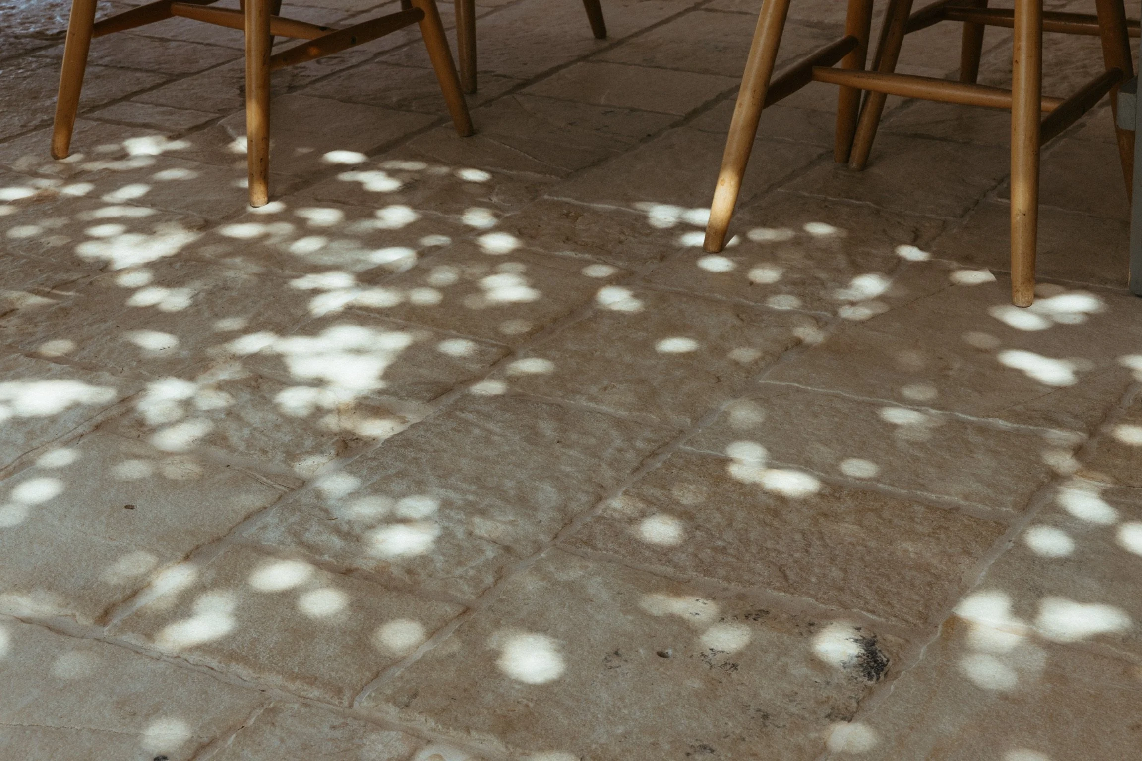 Patterned light and shadow on a tiled restaurant floor with wooden chair legs.