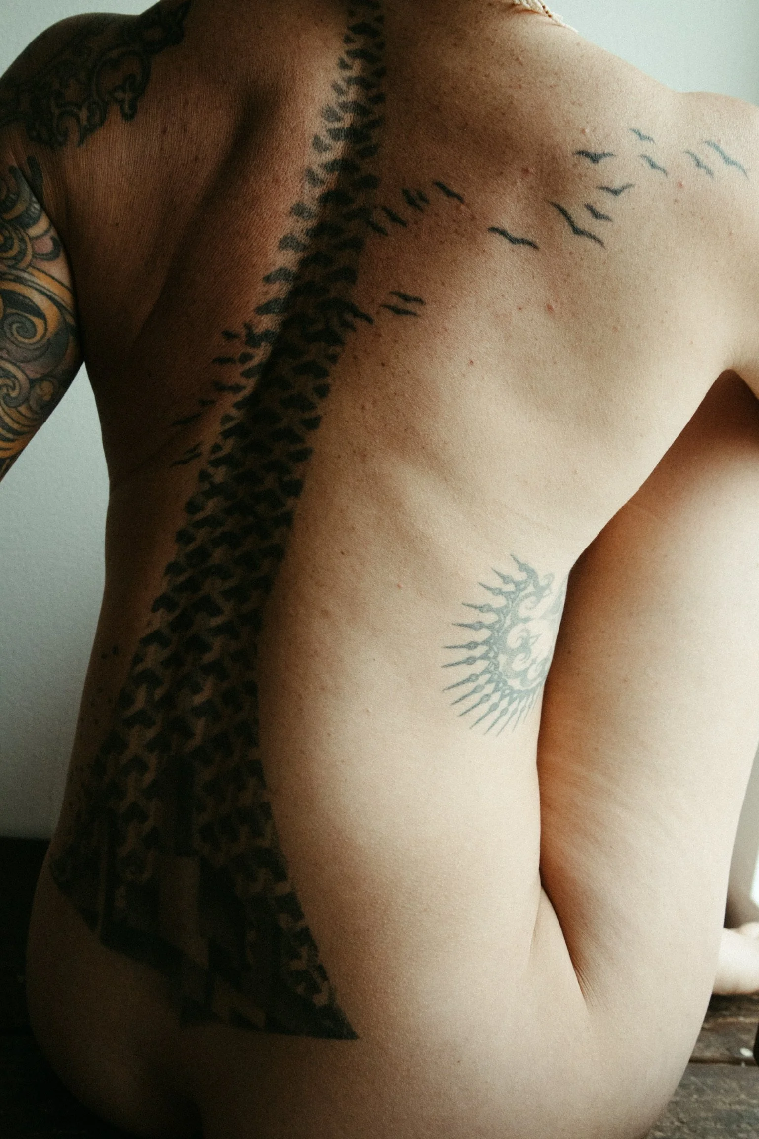 Person's back with tattoos, including abstract designs and patterns along the spine.