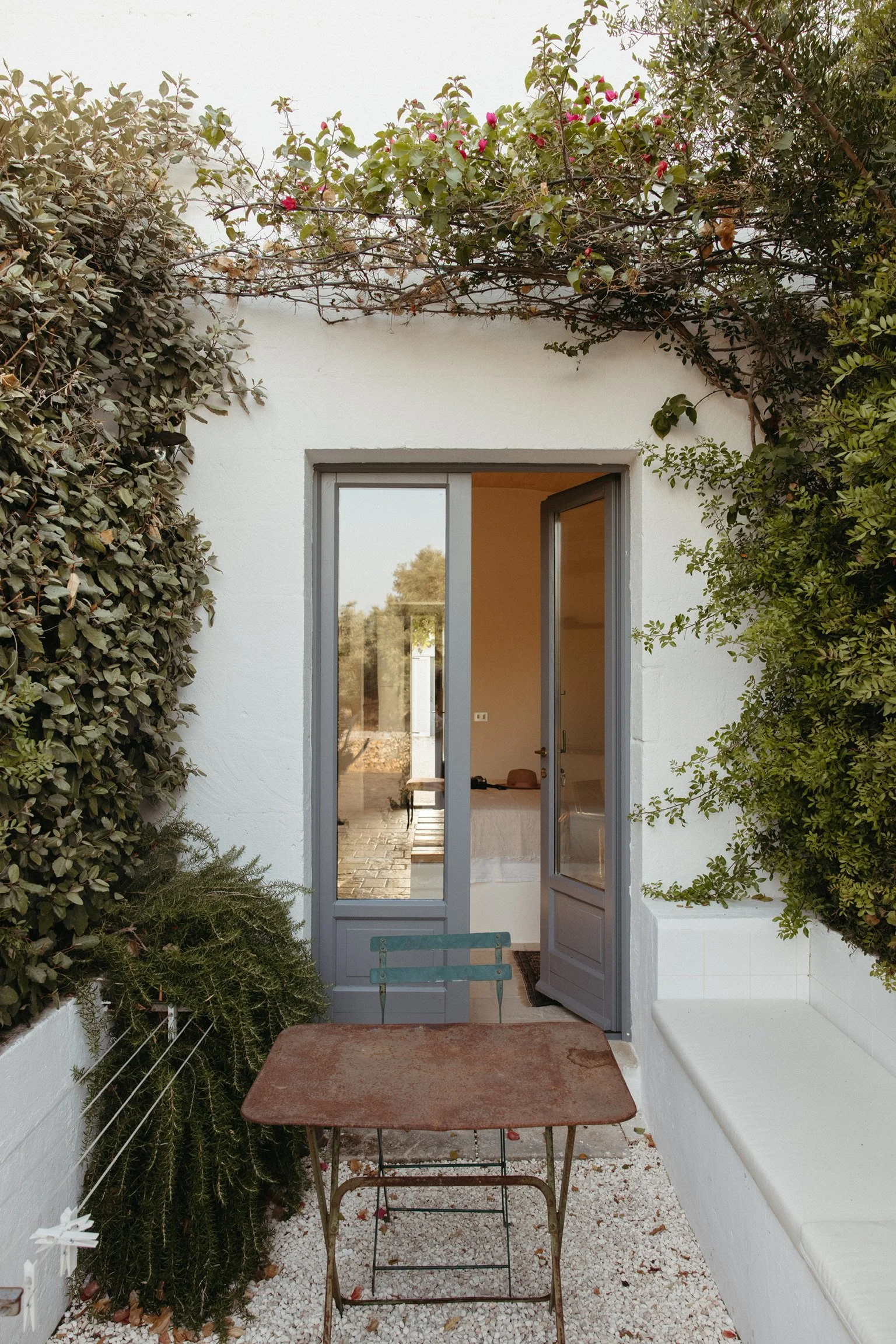 a partially open doorway in the spirit of summer with grapevines framing around the photo. A bistro table invites the guest to sit and stay and read awhile