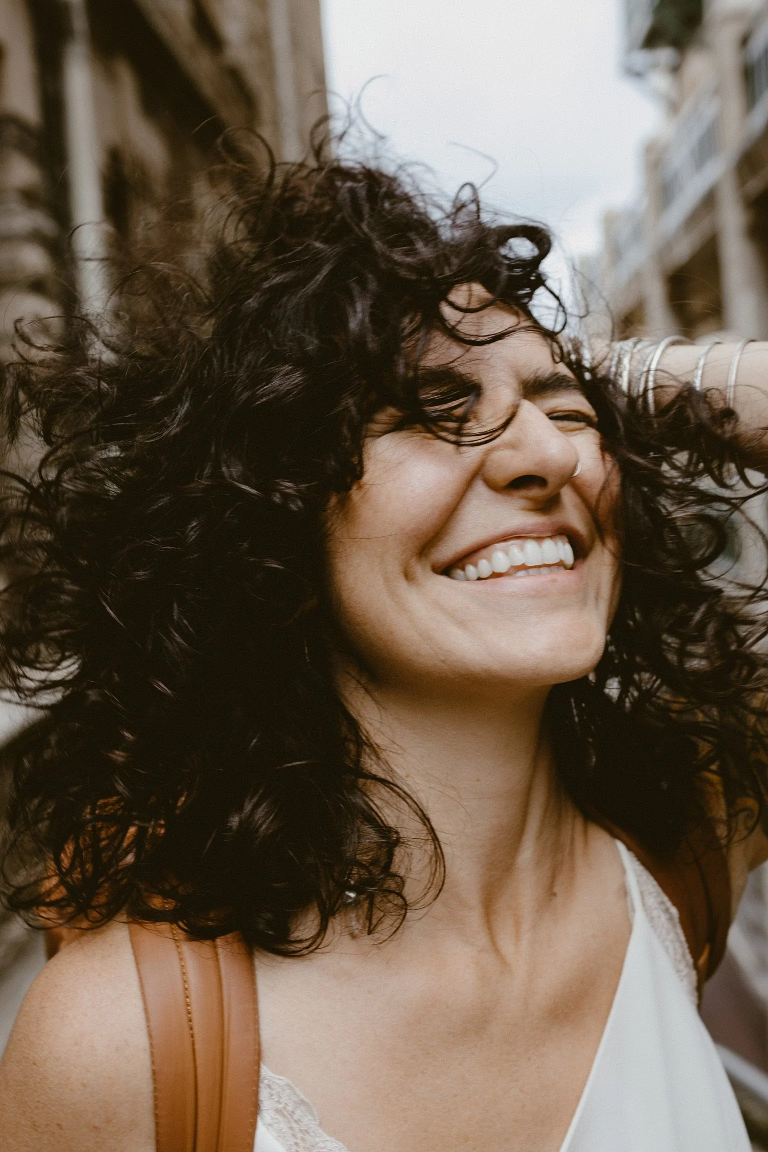 Woman with curly hair smiling outdoors, looking joyful.