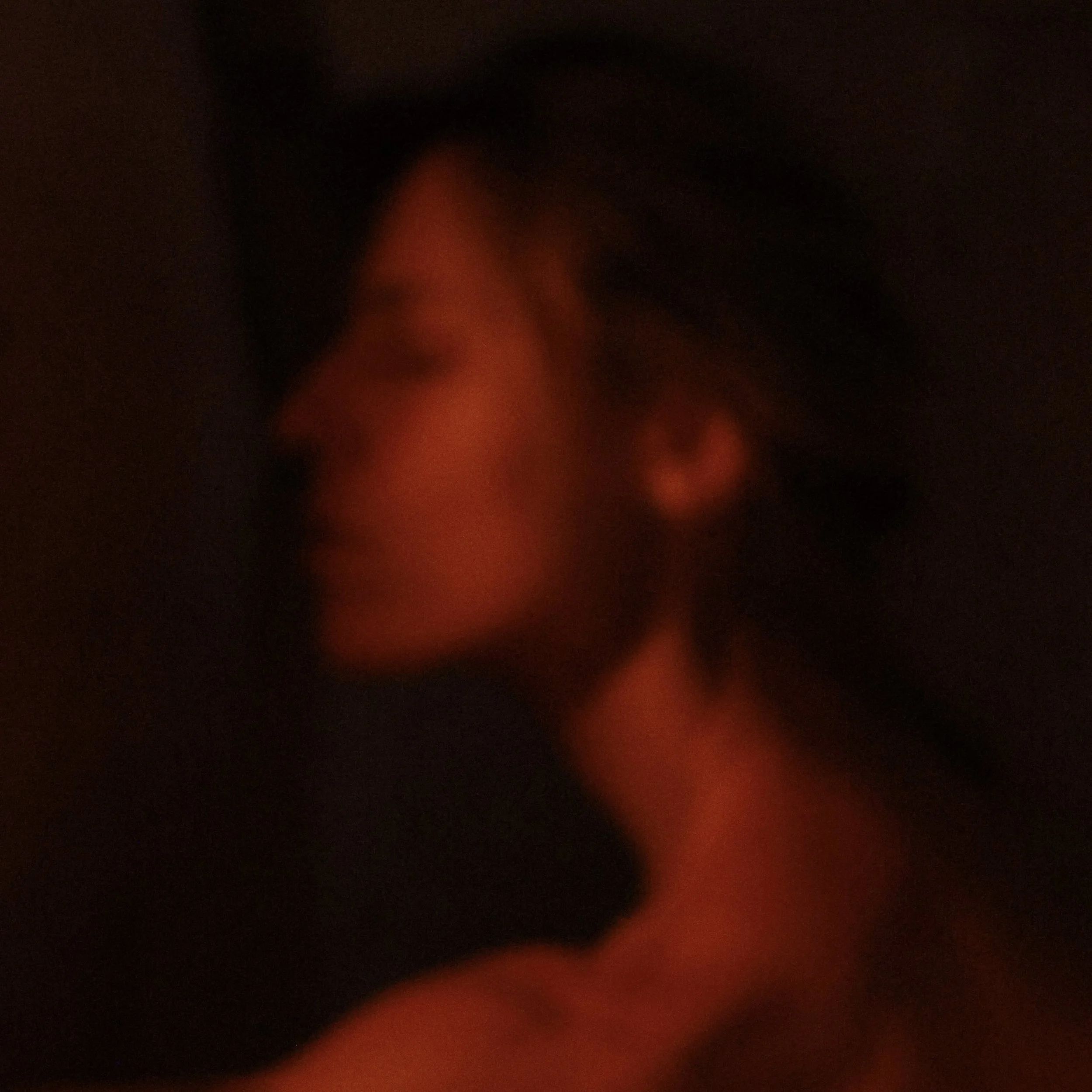Soft focus portrait of a person with closed eyes in dim lighting.