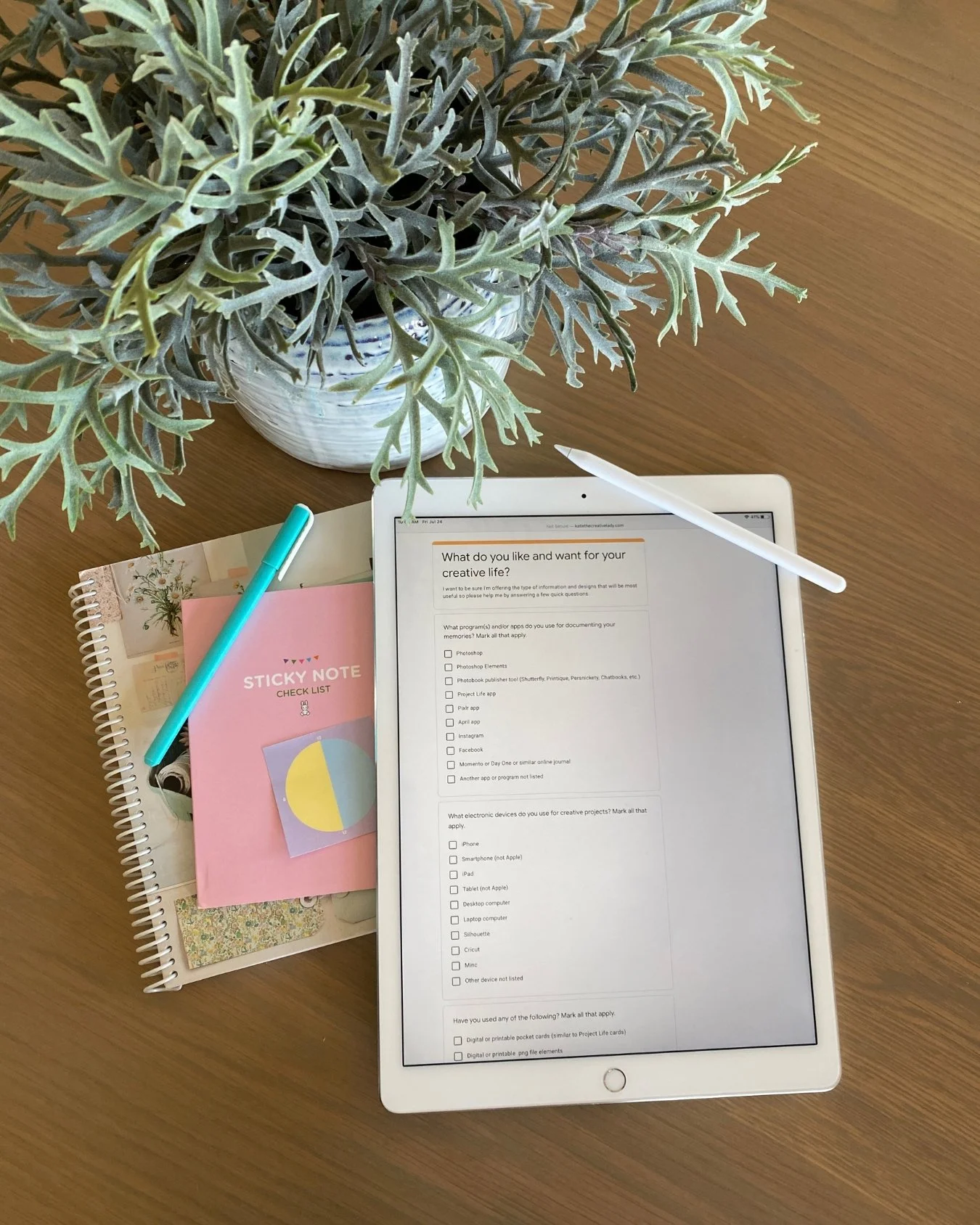 iPad displaying questions about creative interests beside a notebook, checklist, pen, and Apple Pencil on a table.