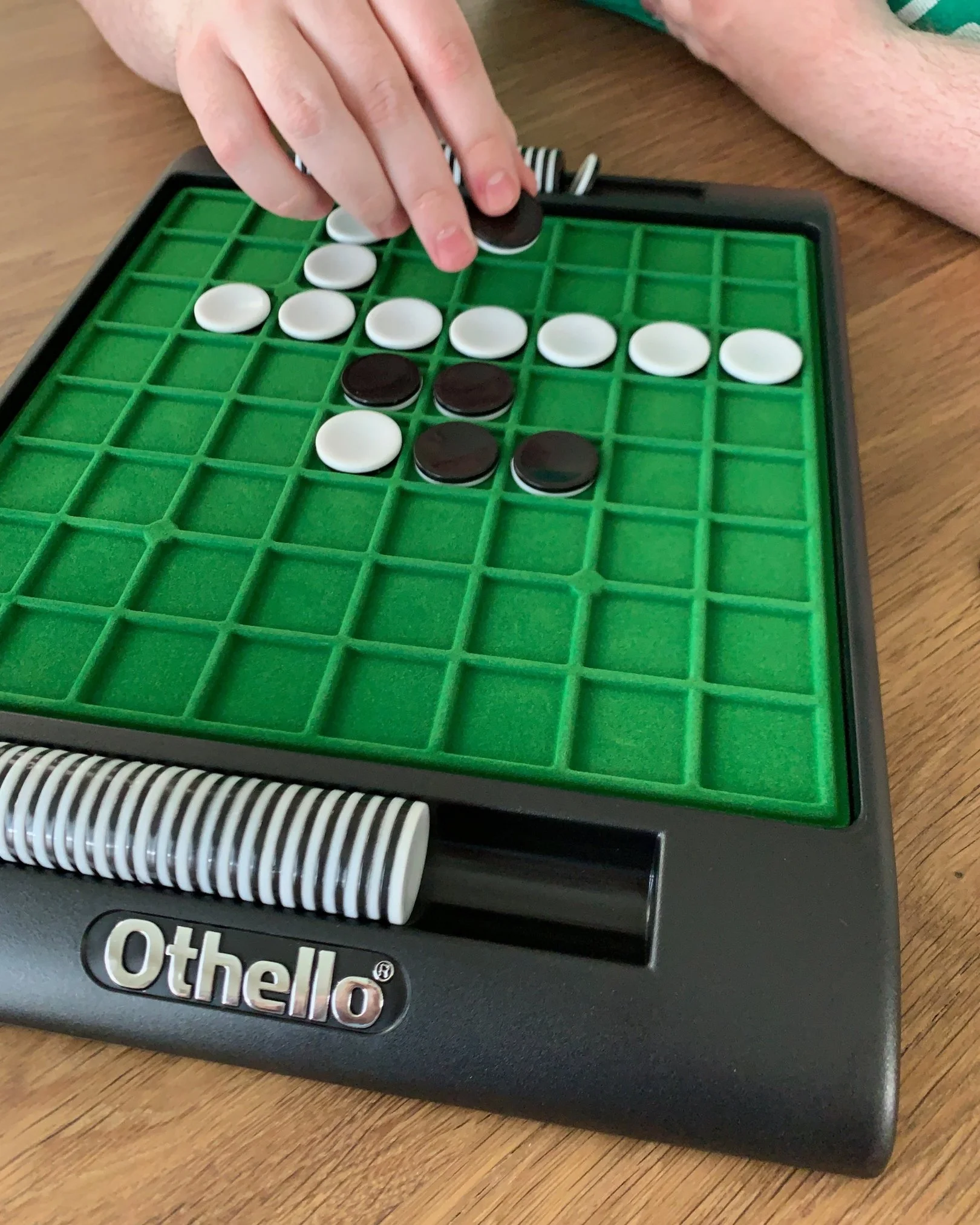 Close-up of hands placing black and white game pieces on an Othello board during a friendly family game.