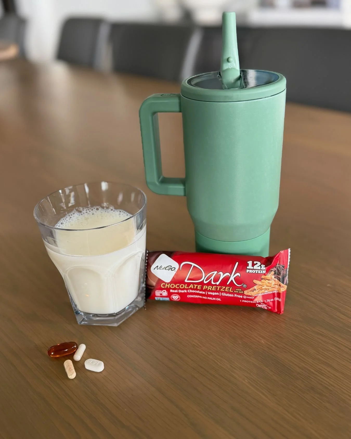 Everyday morning routine with a green tumbler, glass of milk, protein bar, and daily supplements on a dining table.