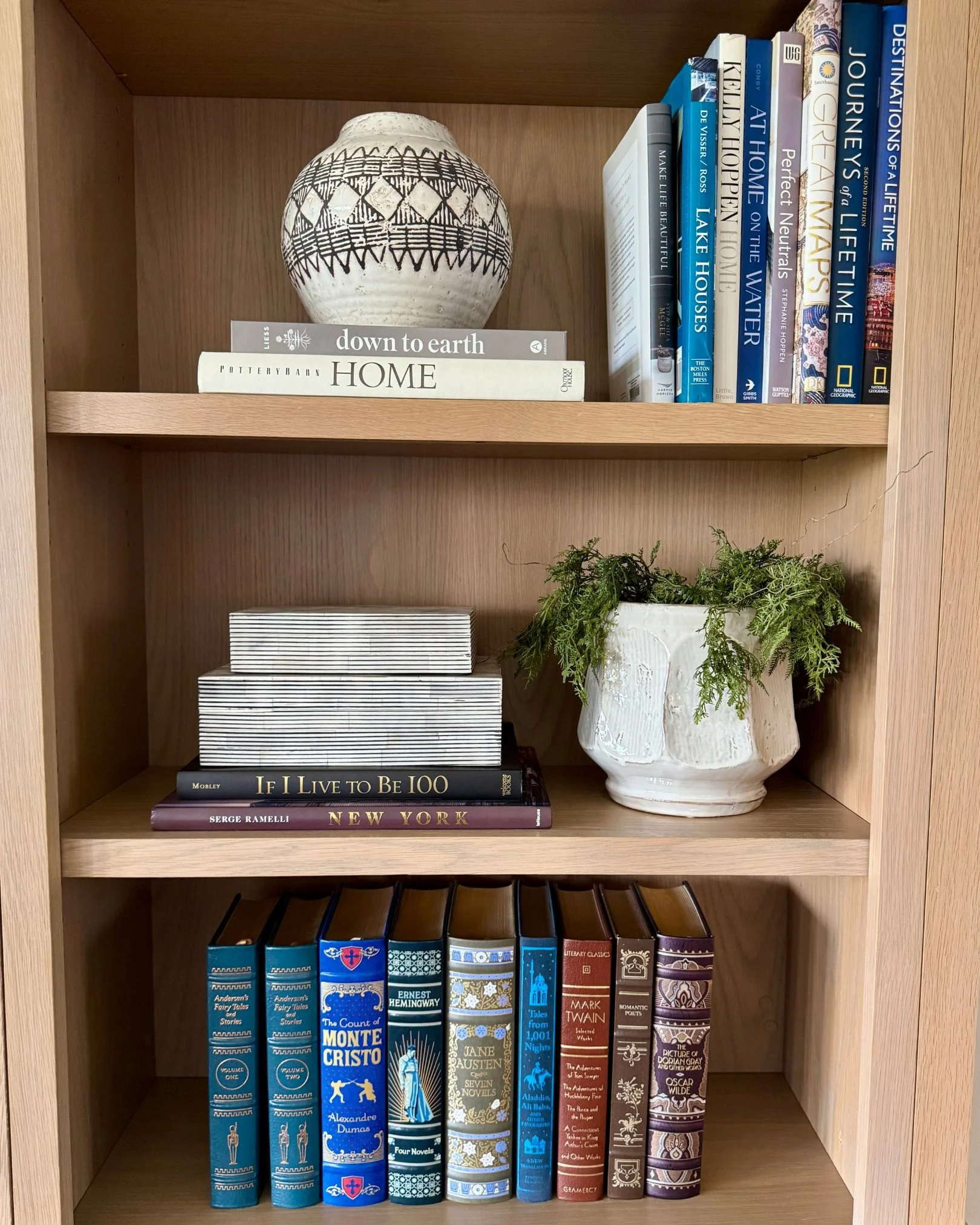 Wooden bookshelf styled with decorative books, pottery, plants, and home decor accents.