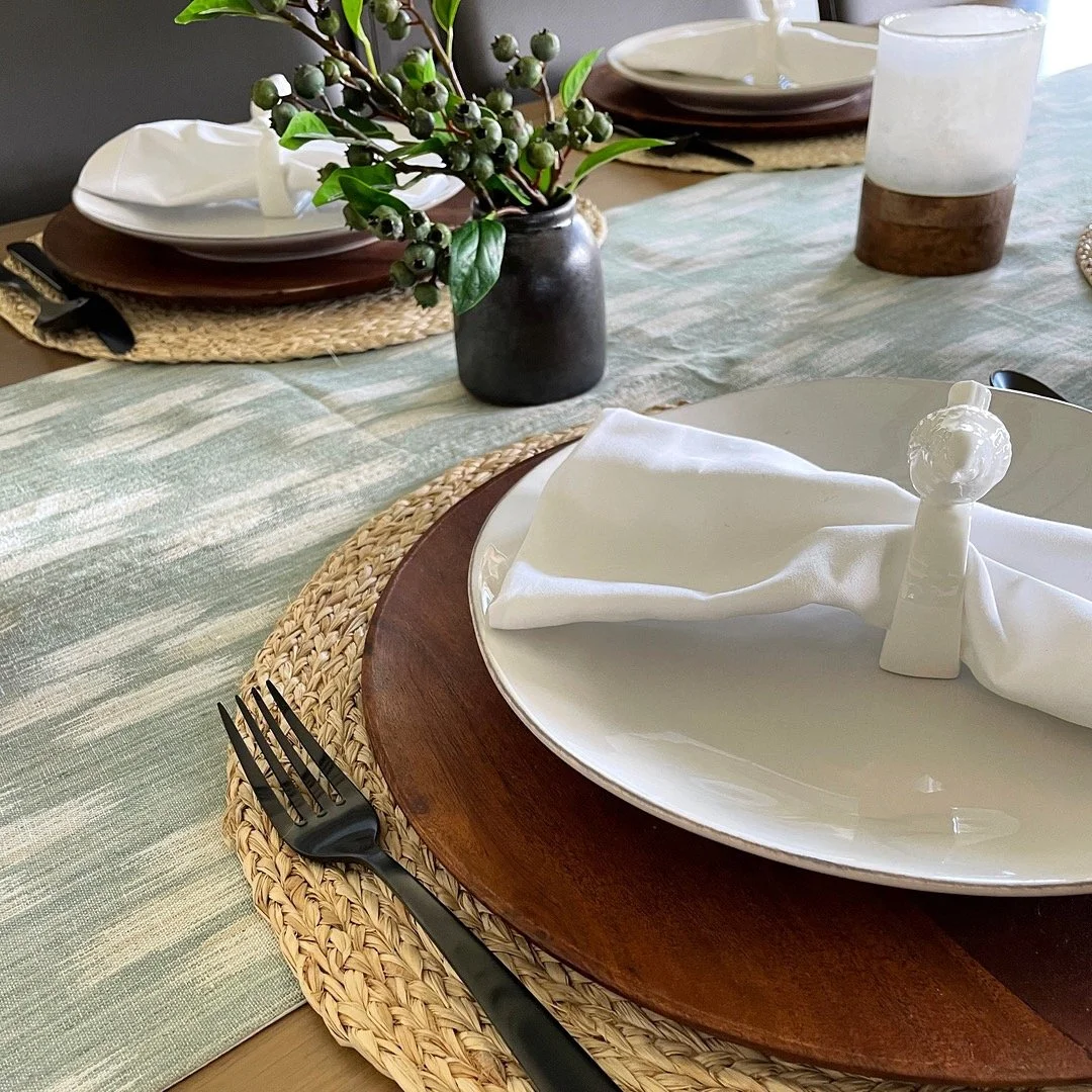 Dining table set for a family meal with white plates, woven placemats, wooden chargers, linen napkins, and a simple centerpiece, capturing an everyday dinner routine.