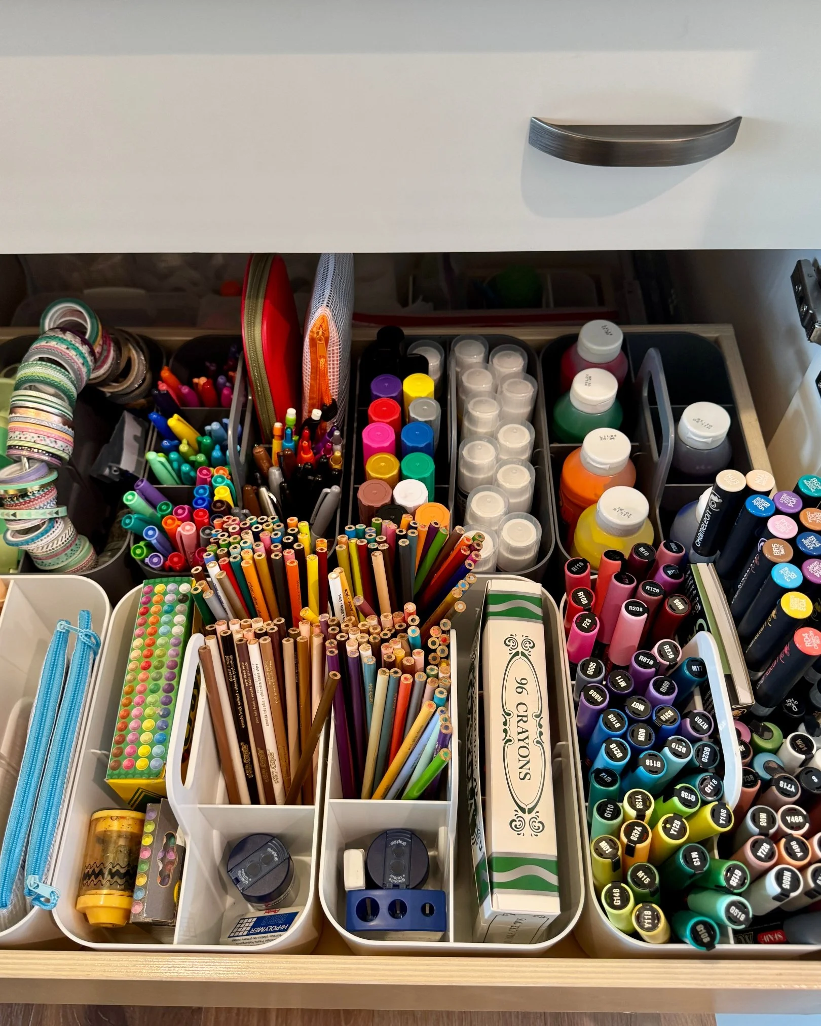 Drawer filled with colorful markers, pencils, paint bottles, washi tape, and organized craft supplies.