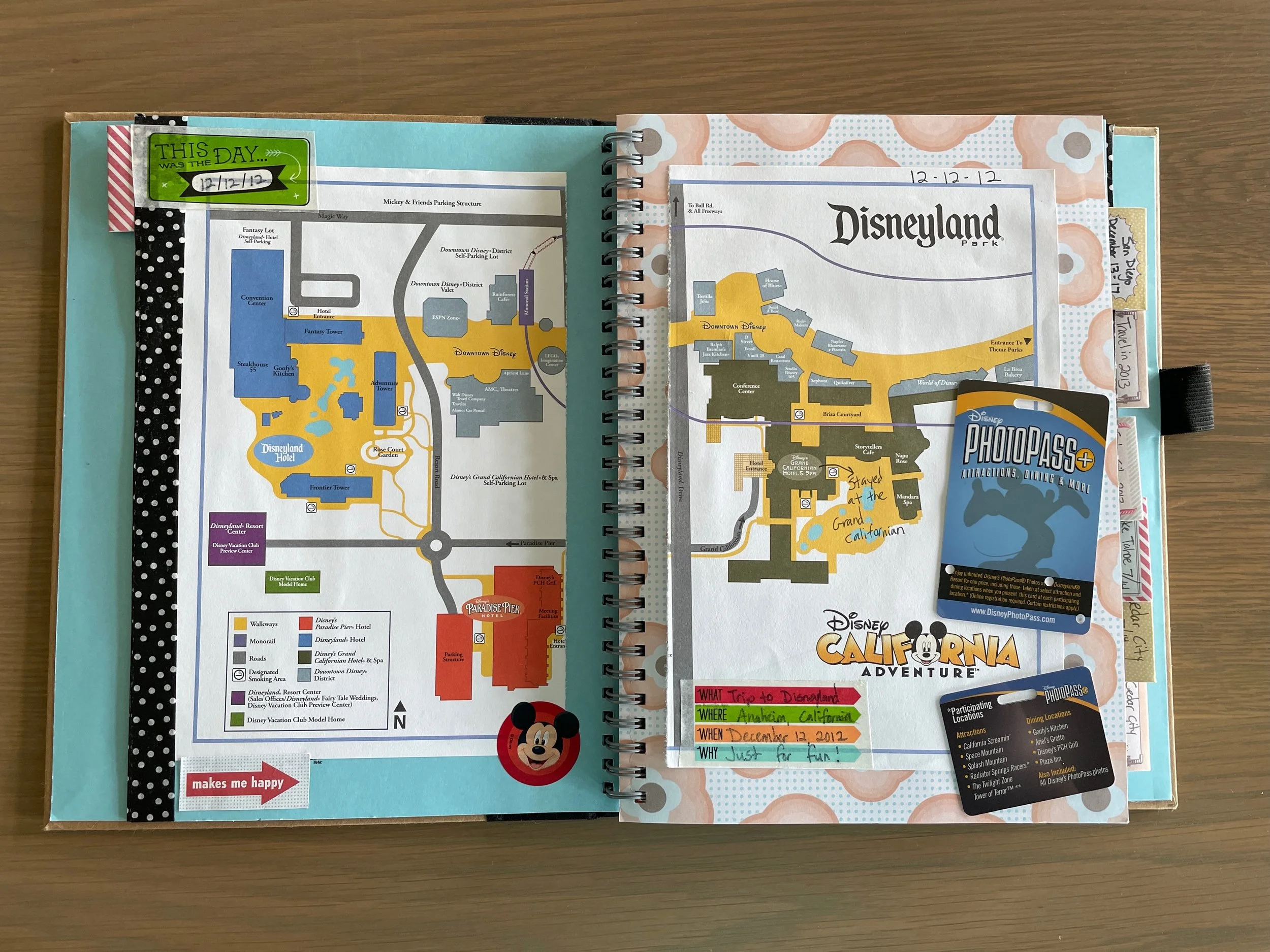 Open spiral-bound travel scrapbook documenting a December 2012 Disneyland trip, featuring Disney park maps, PhotoPass cards, handwritten journaling, and colorful scrapbook embellishments