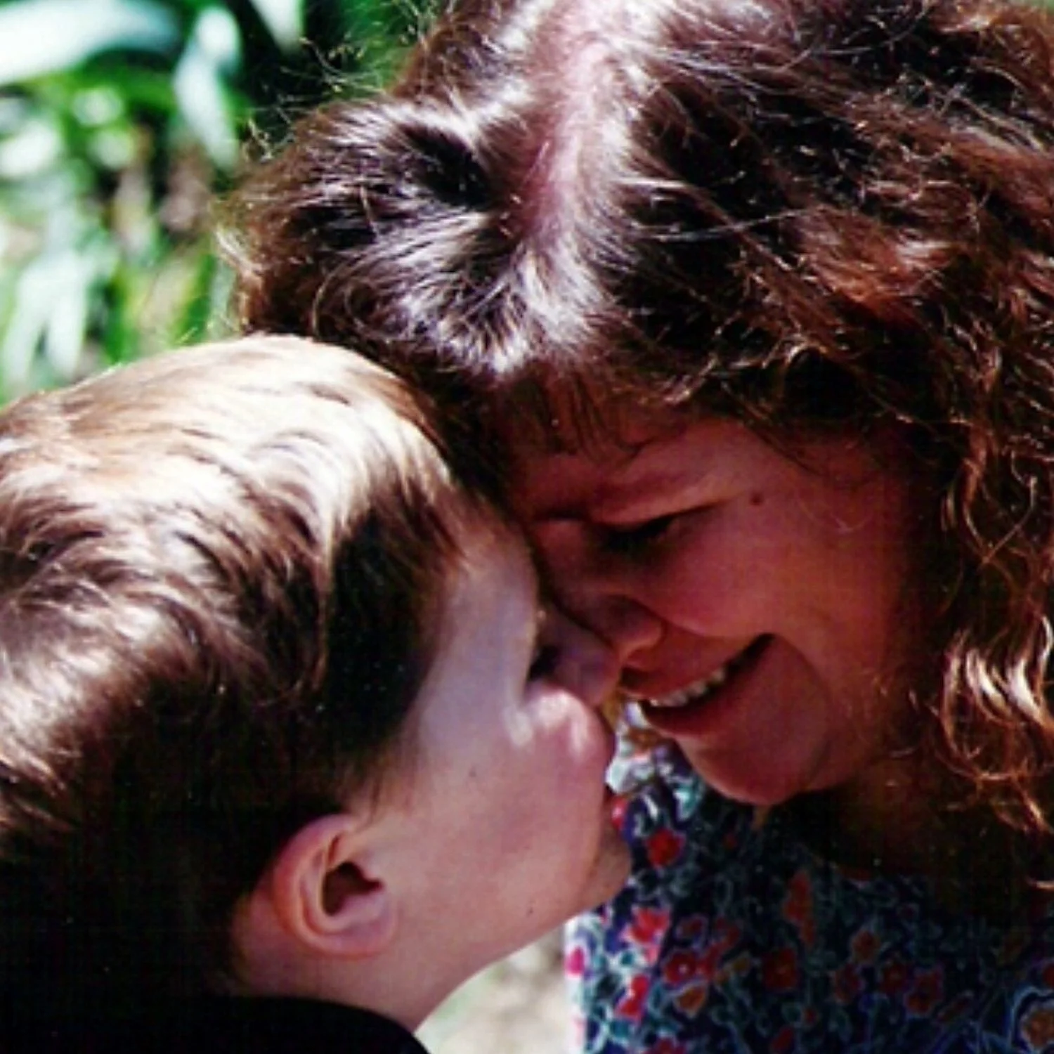 Mother and son sharing a close, affectionate moment with their foreheads touching and smiling.