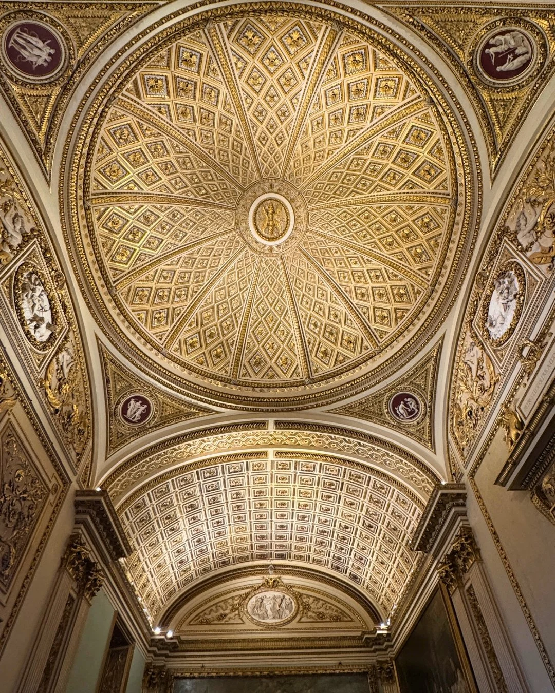 Elaborately decorated ceiling featuring intricate gold geometric patterns, a circular vaulted design, and classical architectural details.