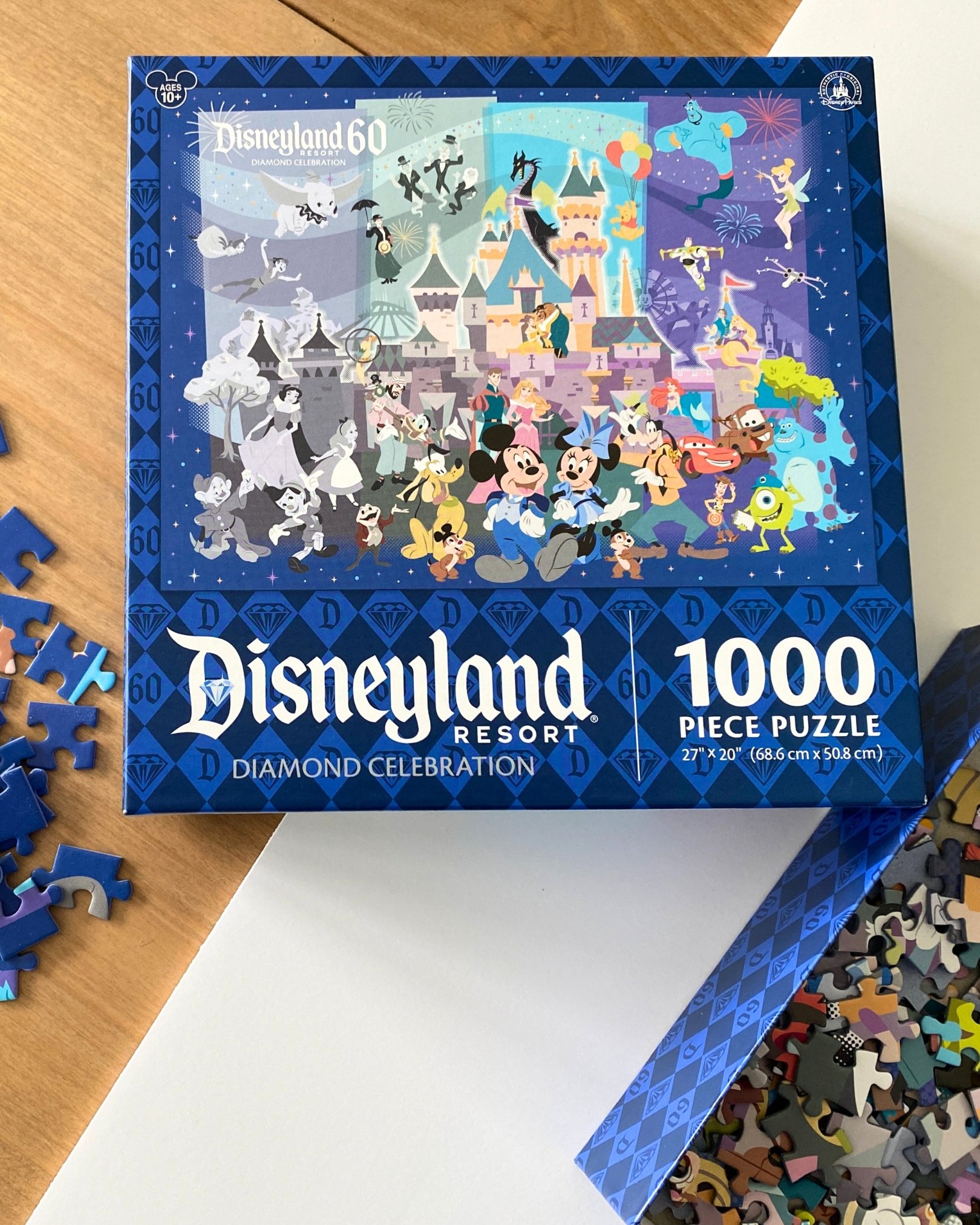 Disneyland Resort Diamond Celebration 1,000-piece puzzle box surrounded by puzzle pieces on a table, ready for a fun family activity.