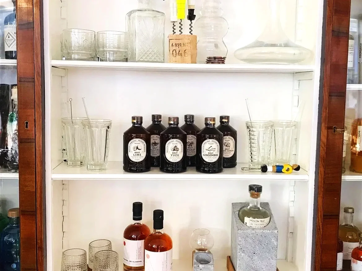 Étagère effet marbre clair avec diverses bouteilles de spiritueux et verres, dont de la vodka, du gin, du whisky, et des accessoires