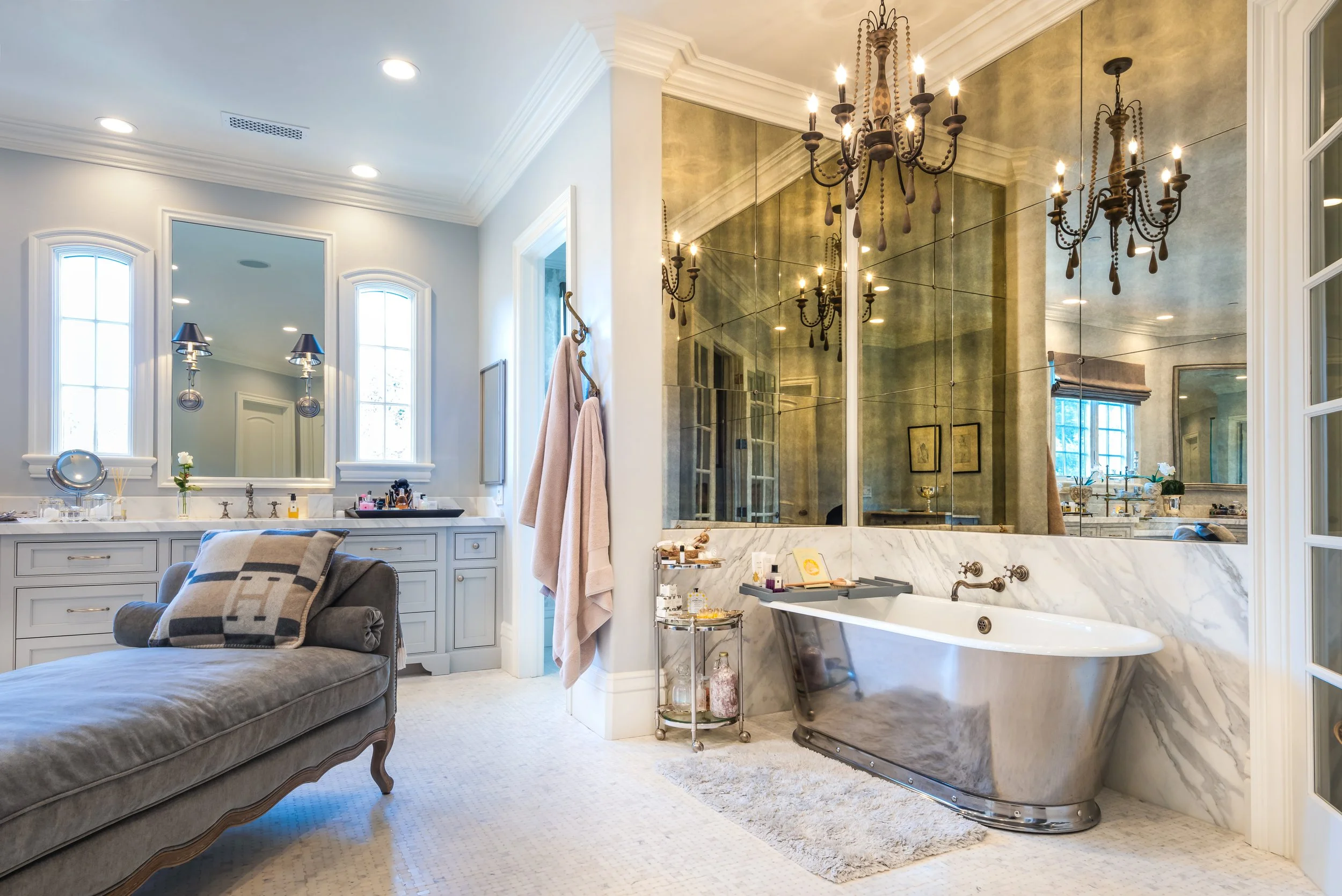 Luxurious bathroom with a vintage clawfoot bathtub, a large mirror, chandeliers, and a vanity with makeup accessories.