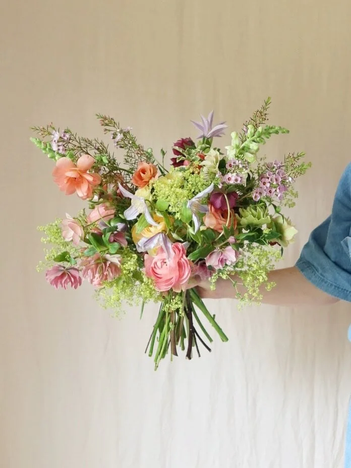 A person in a blue shirt holding a colorful bouquet of mixed flowers.